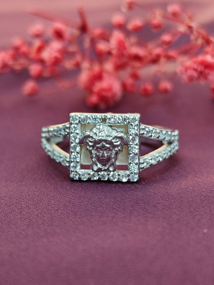 Silver ring with a lion emblem design on a purple surface with red flowers in the background
