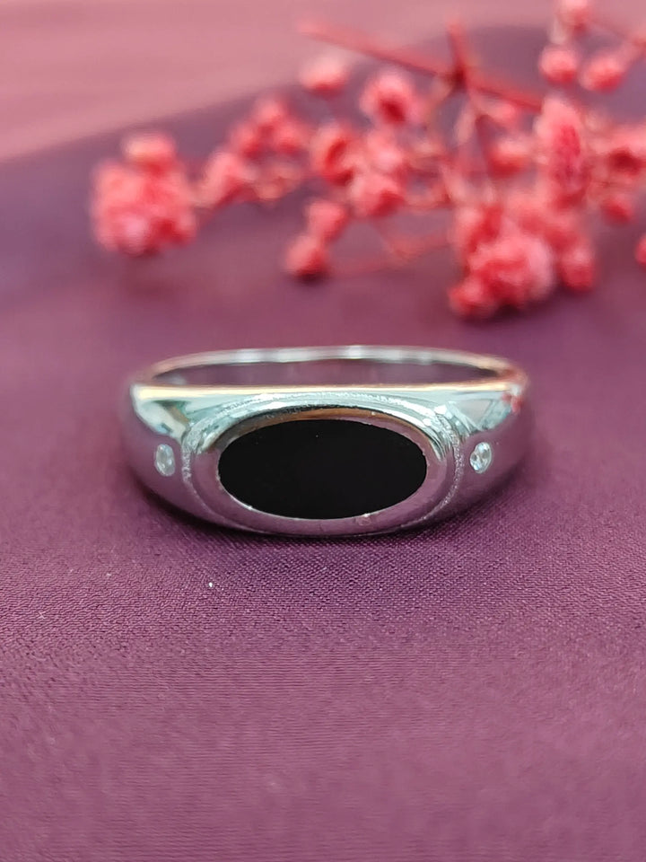 Silver ring with a black stone on a purple surface with red flowers.