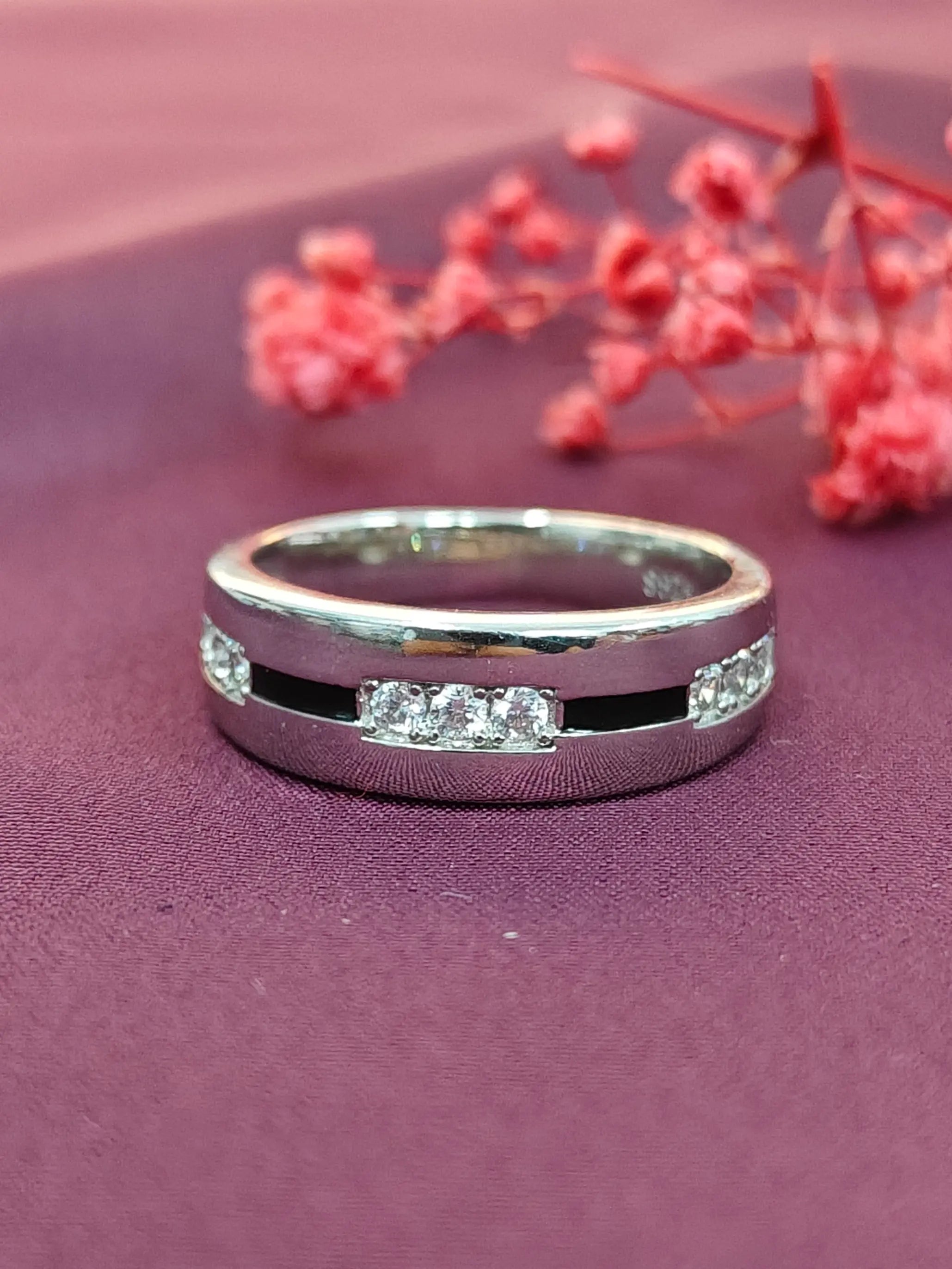 Silver ring with embedded diamonds on a purple surface with red flowers.