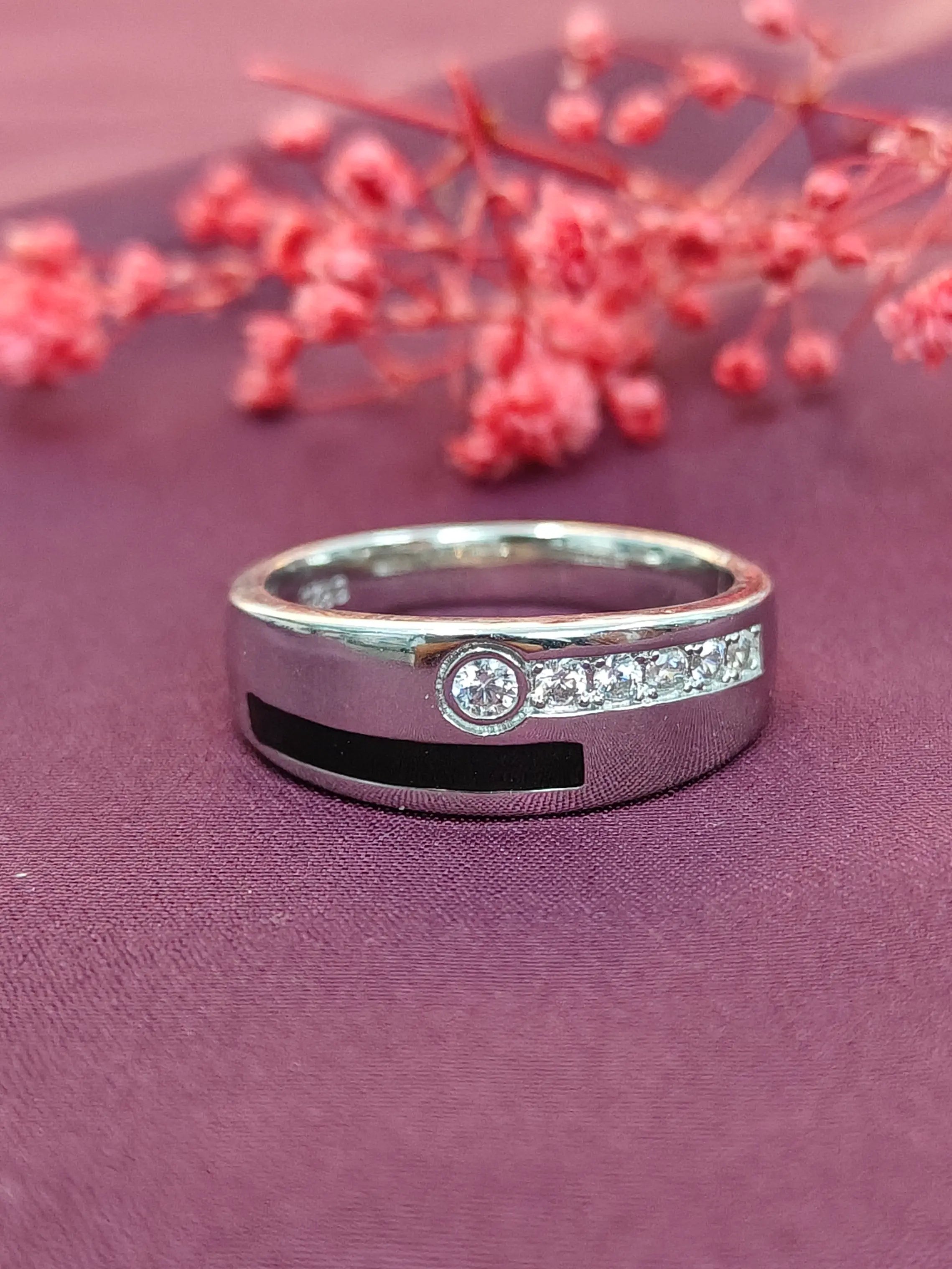 Silver ring with black and white accents on a purple surface with pink flowers.