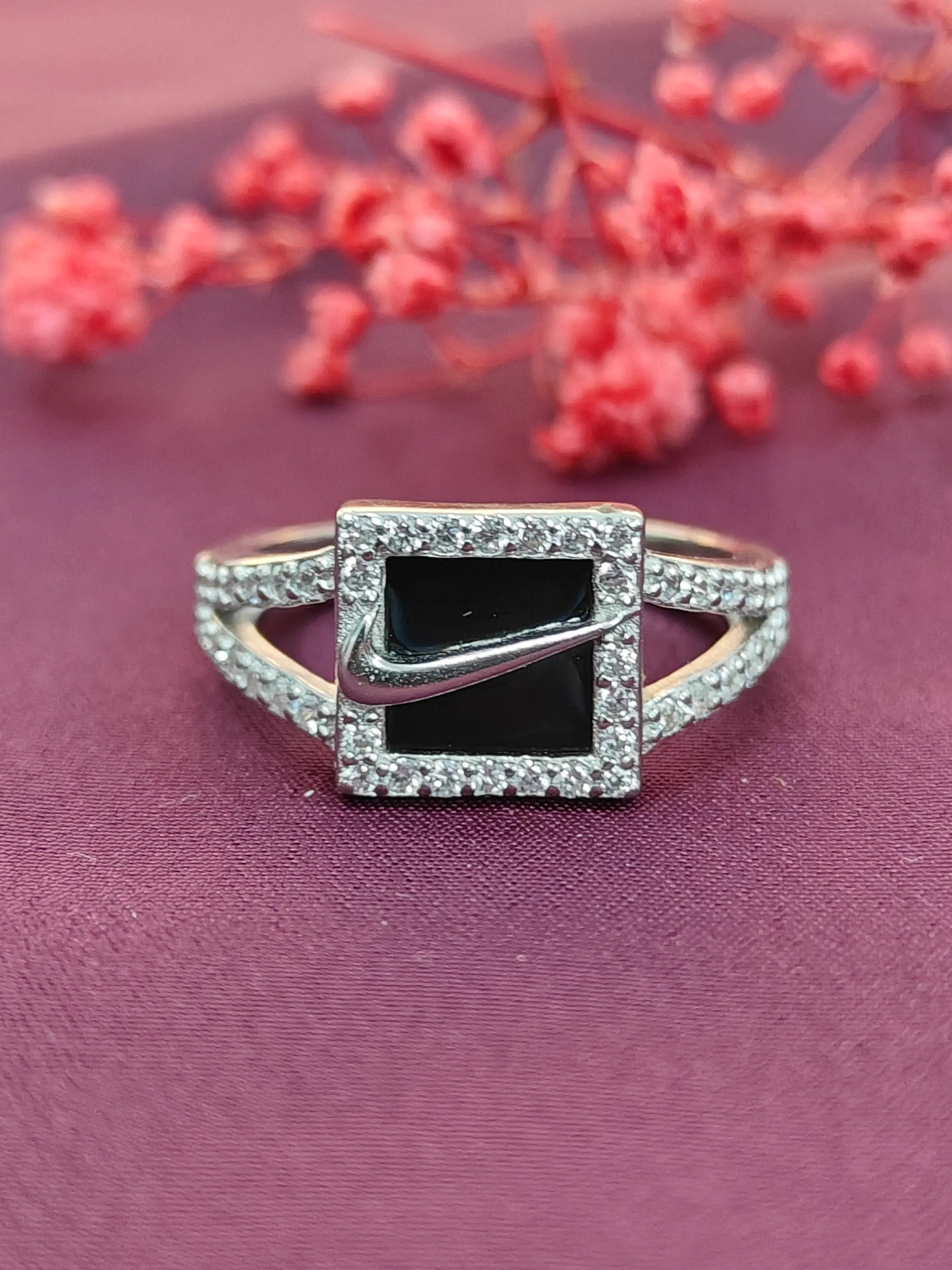 Silver ring with a black gemstone and diamond accents on a purple fabric background with red flowers.