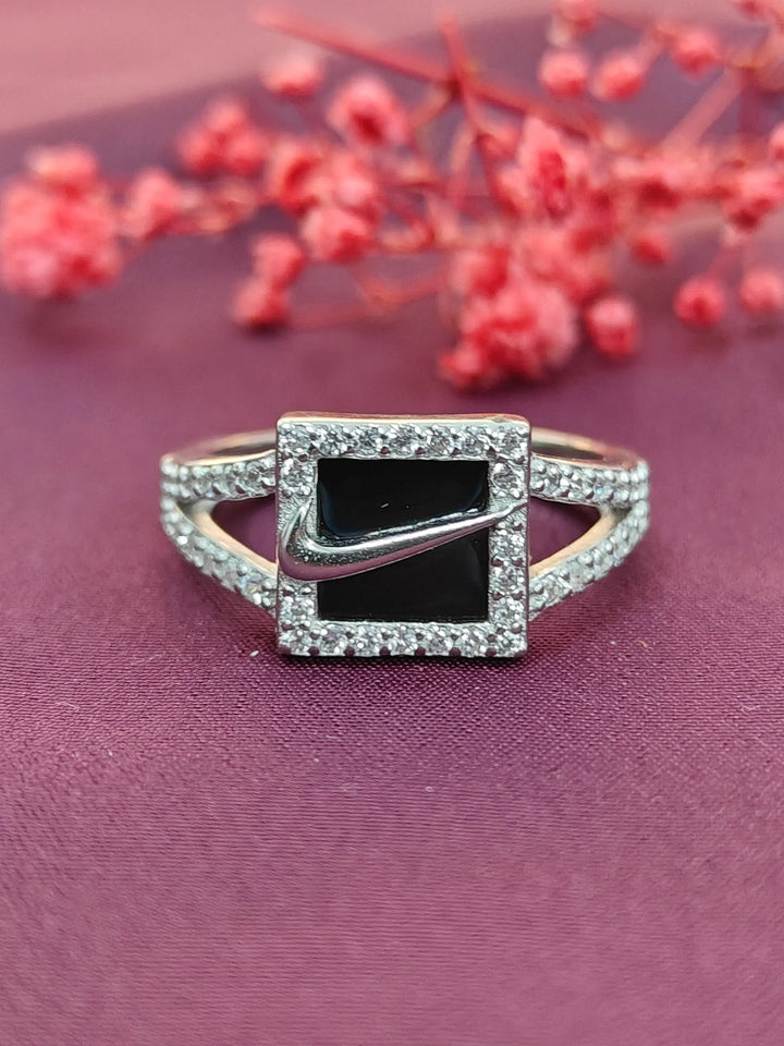 Silver ring with a black gemstone and diamond accents on a purple fabric background with red flowers.