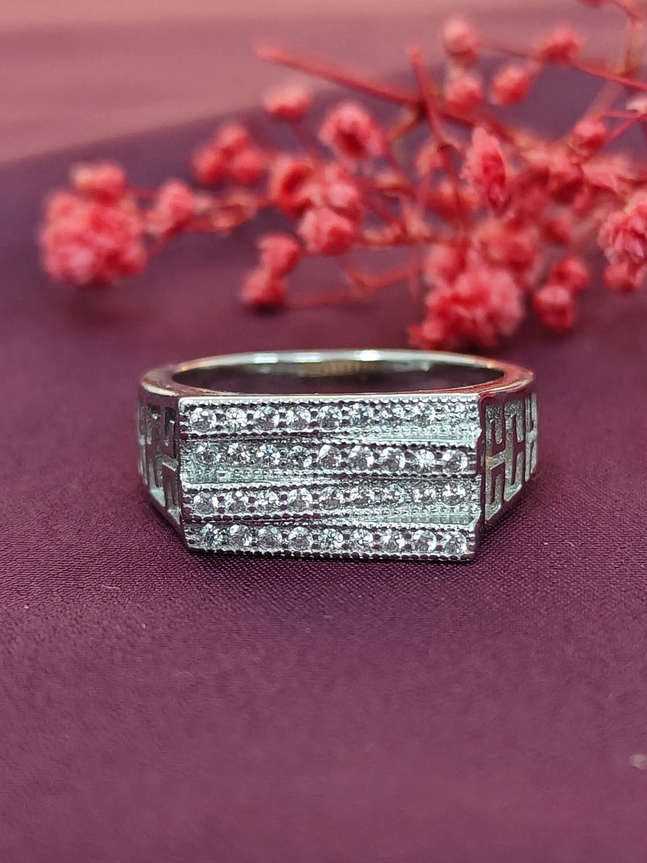 Silver ring with diamond accents on a purple surface with red flowers in the background