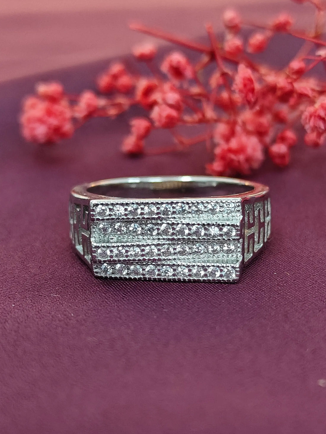 Silver ring with diamond accents on a purple surface with red flowers in the background