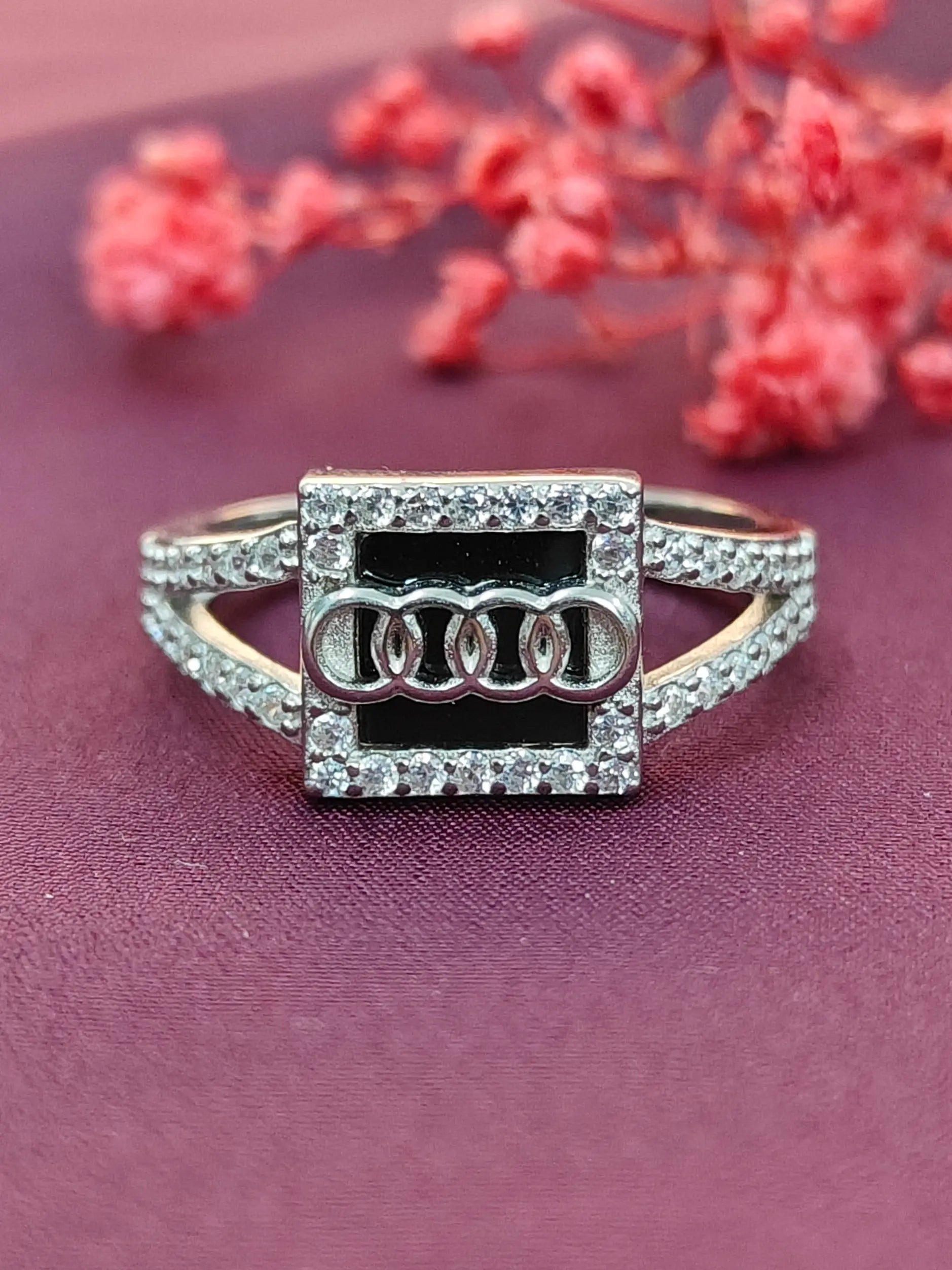 Silver ring with Audi logo on a pink background with red flowers