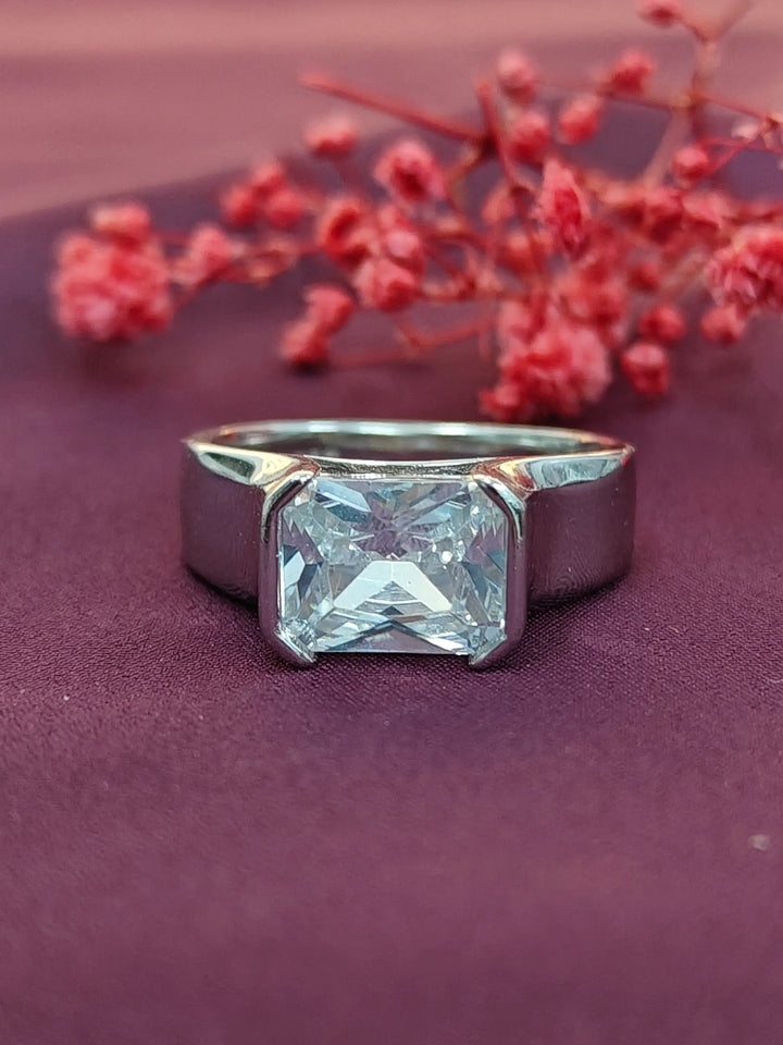 Silver ring with a large diamond on a purple surface with red flowers in the background