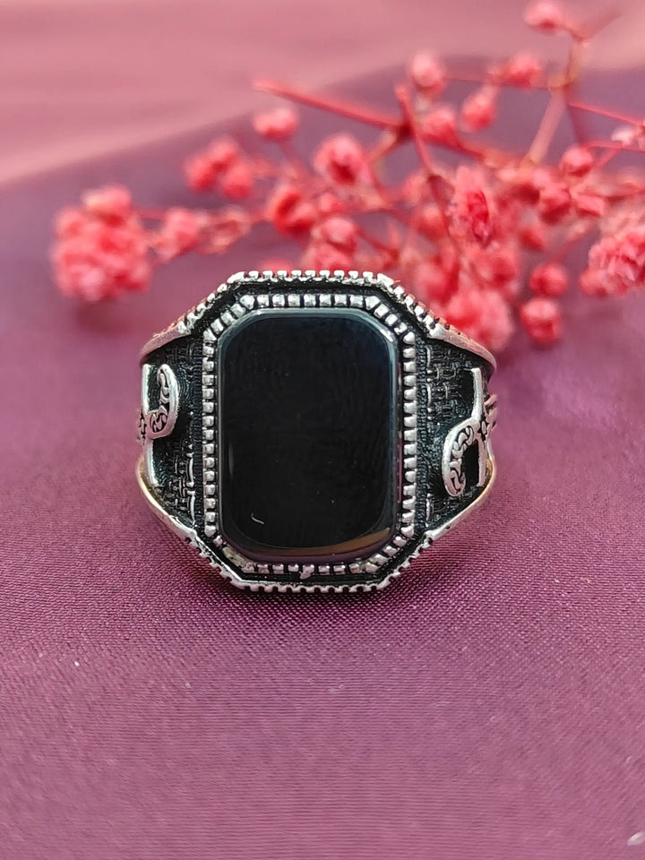 Silver ring with a black stone on a pink fabric background with red flowers.