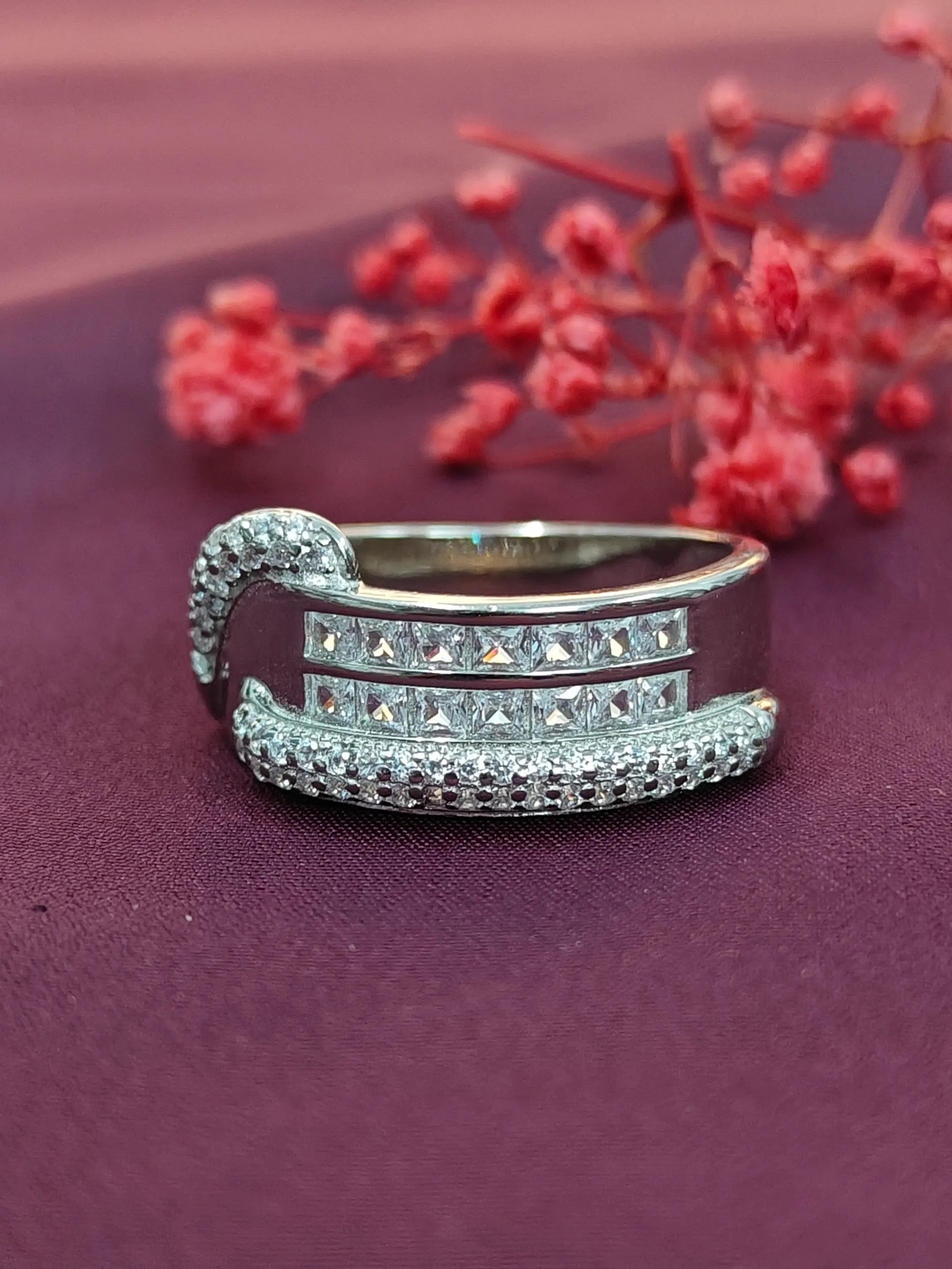 Silver ring with gemstones on a purple surface with red flowers in the background