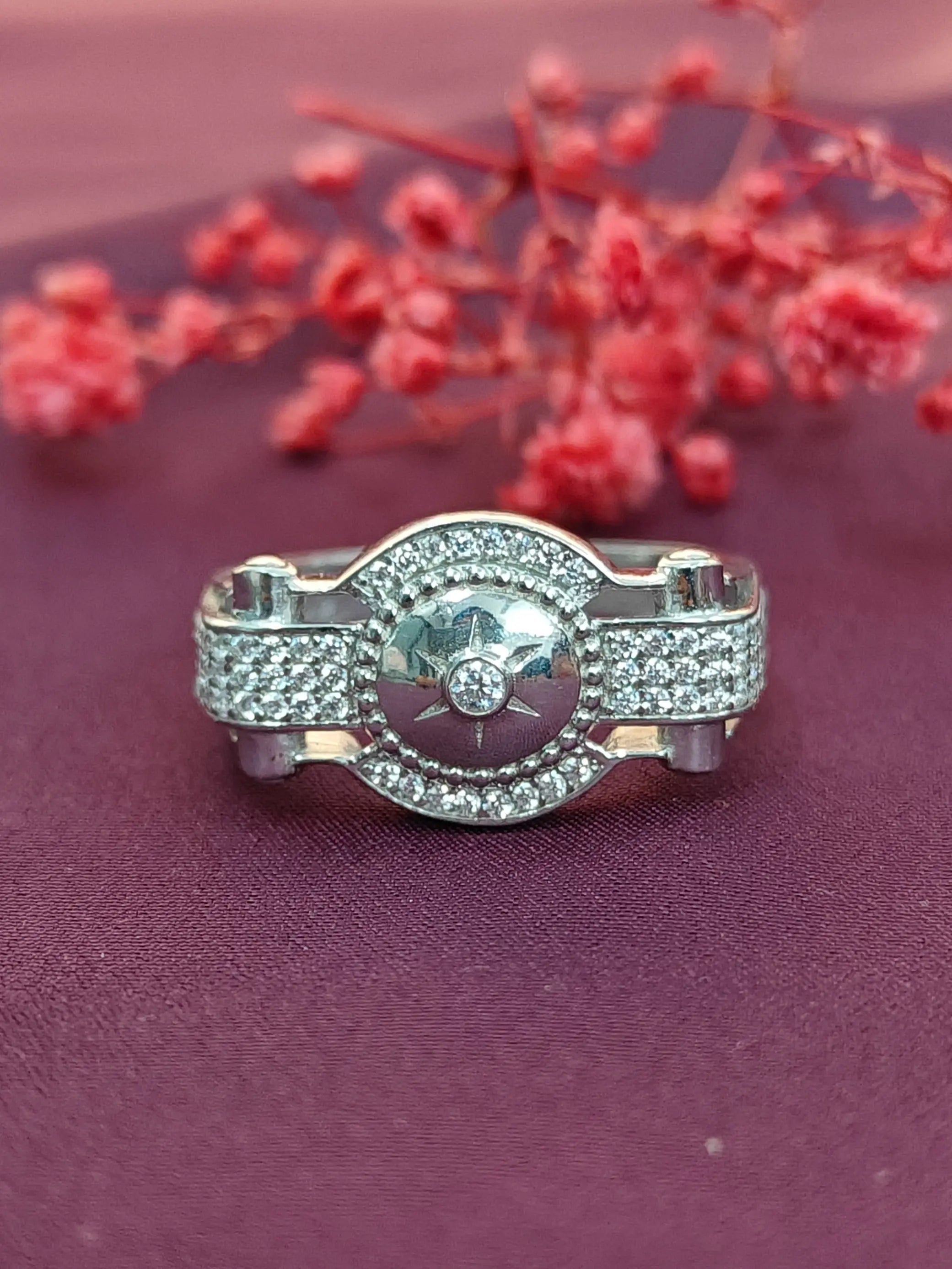 Silver ring with gemstones on a purple surface with red flowers in the background
