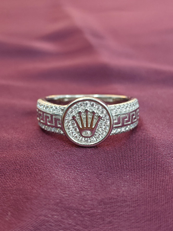 Silver ring with a central emblem on a purple fabric background