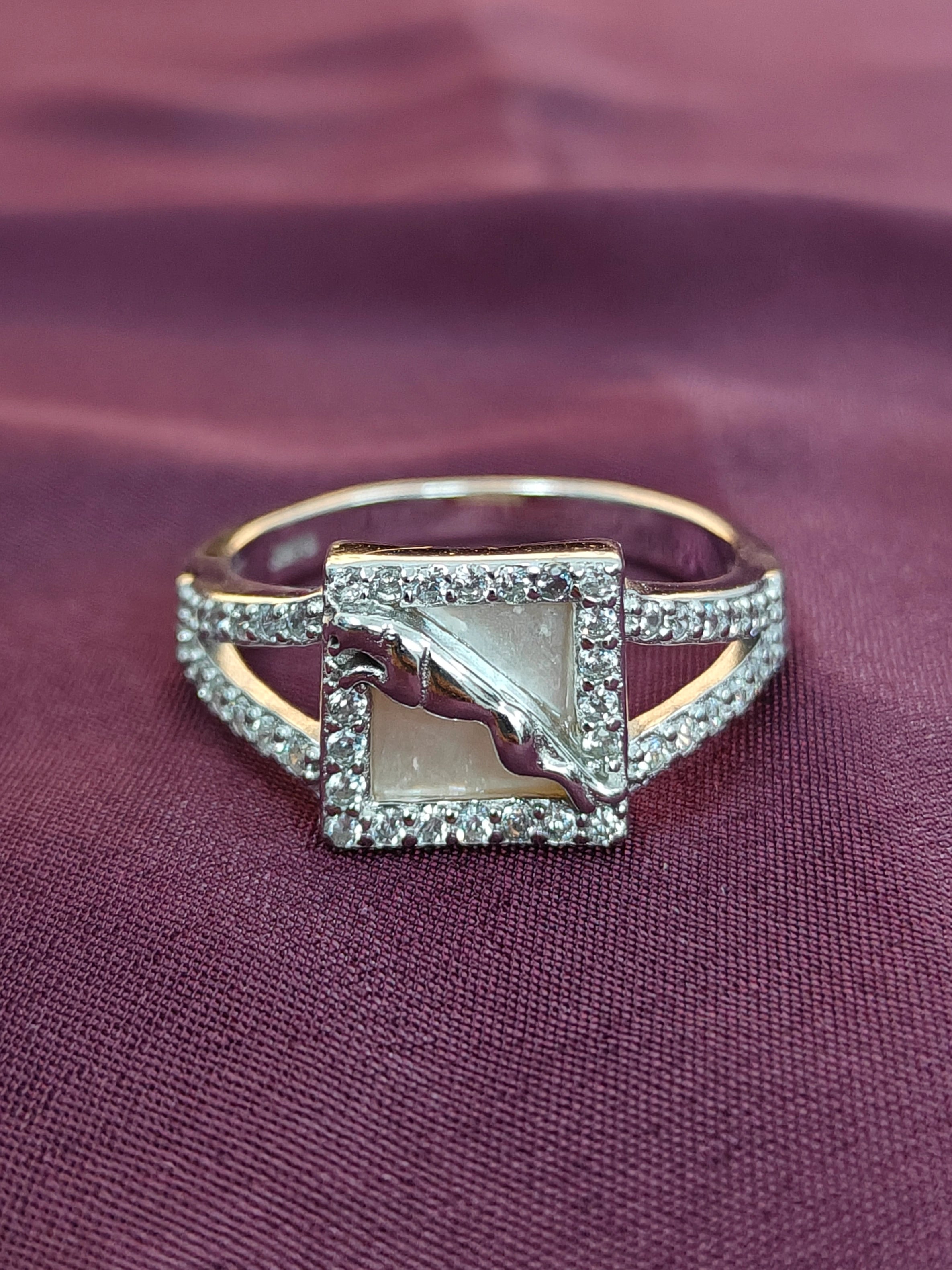 Gold ring with a square stone and diamond accents on a purple fabric background