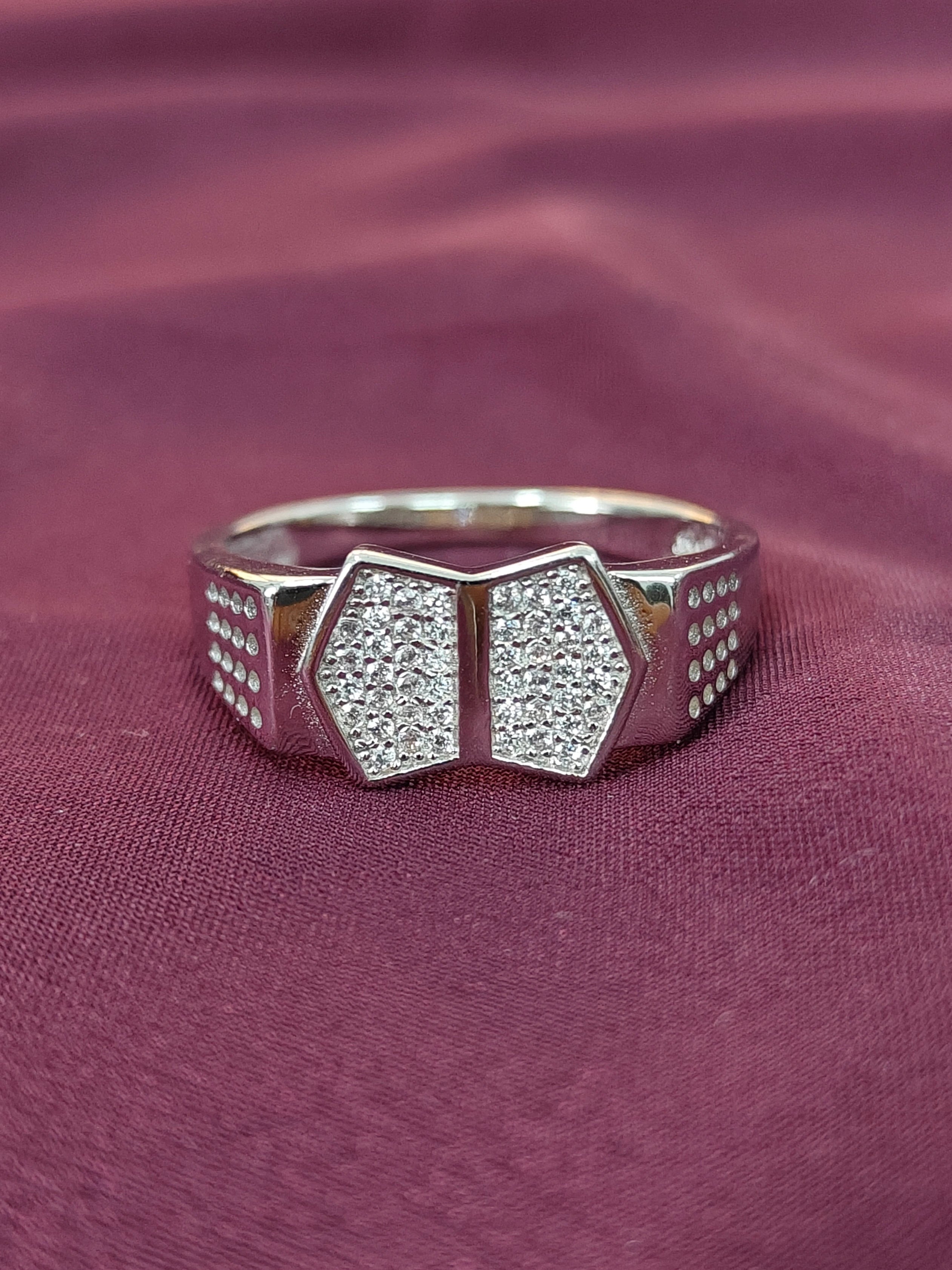 Silver ring with hexagonal design and embedded stones on a maroon fabric background