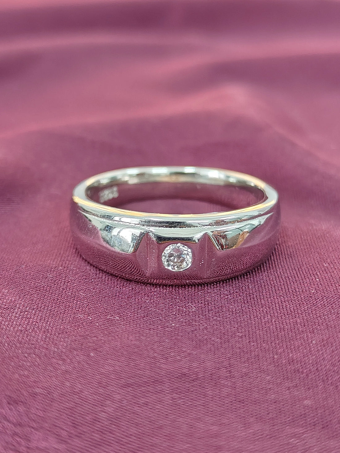 Silver ring with a diamond on a purple fabric background