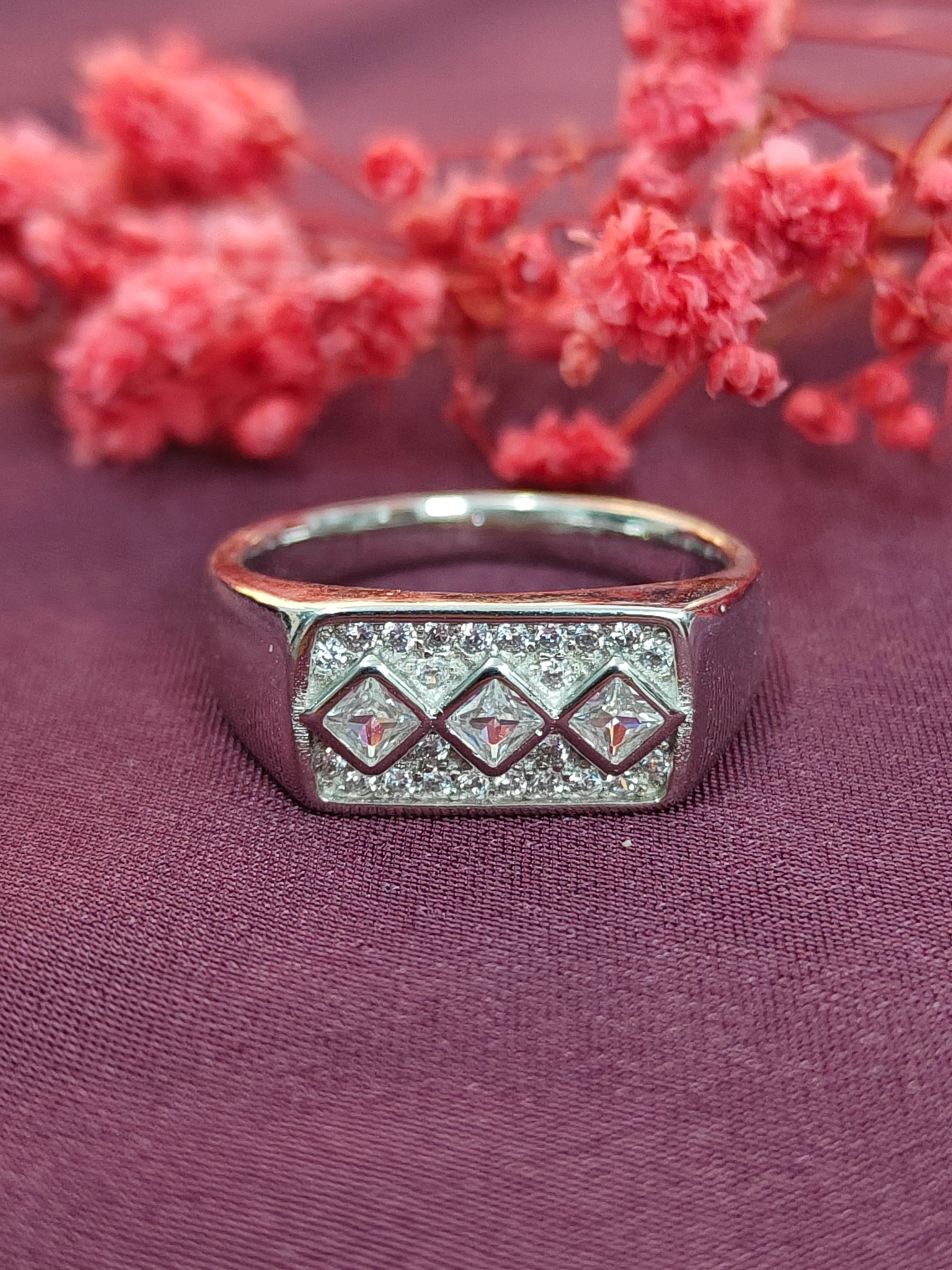 Silver ring with diamond-like stones on a purple fabric background with pink flowers.