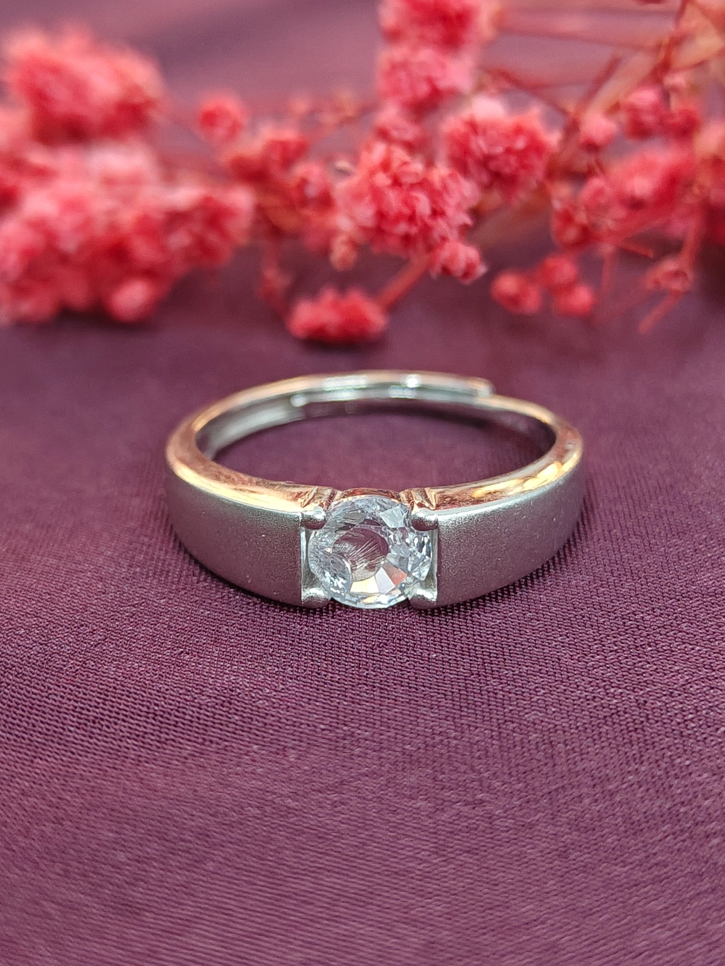 Silver ring with a diamond on a purple fabric background with pink flowers.