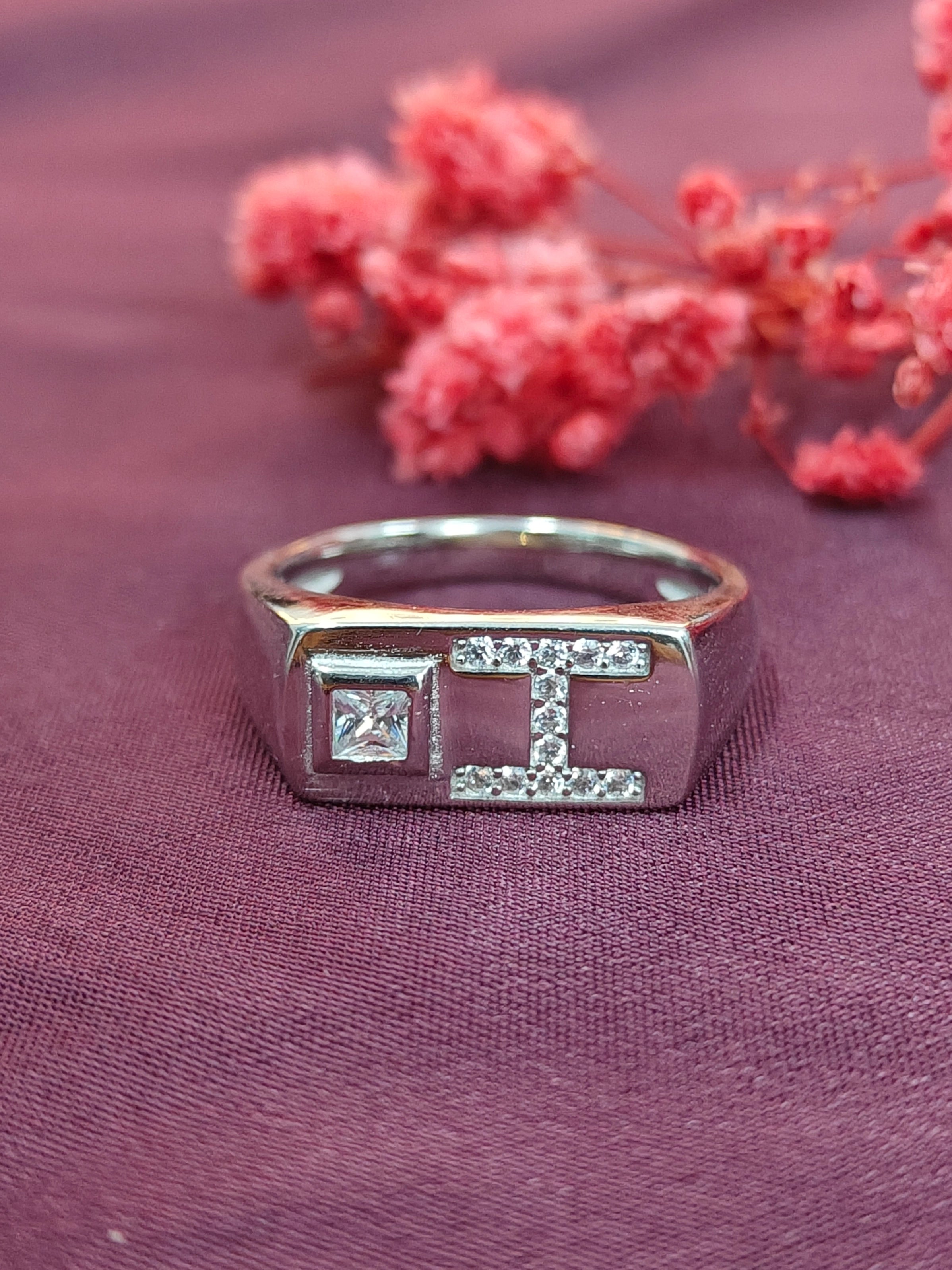 Silver ring with a design on a purple fabric background with pink flowers.