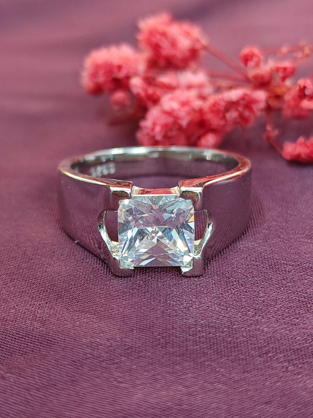 Silver ring with a large diamond on a purple fabric background with pink flowers.