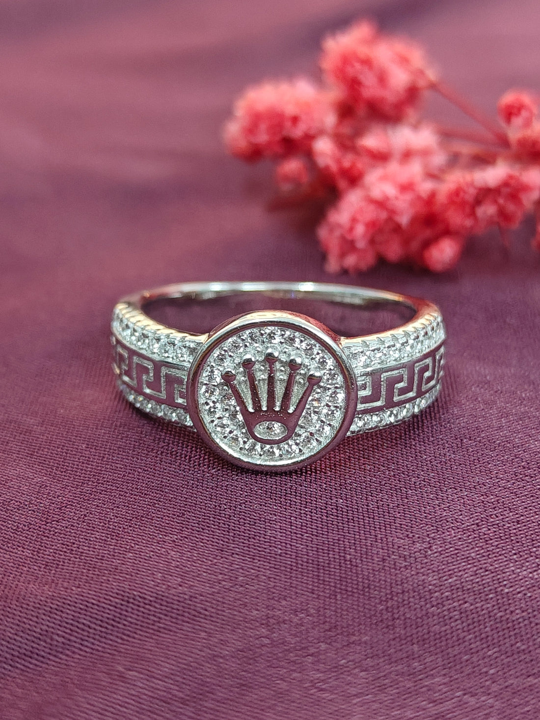 Silver ring with a prominent logo on a purple fabric background