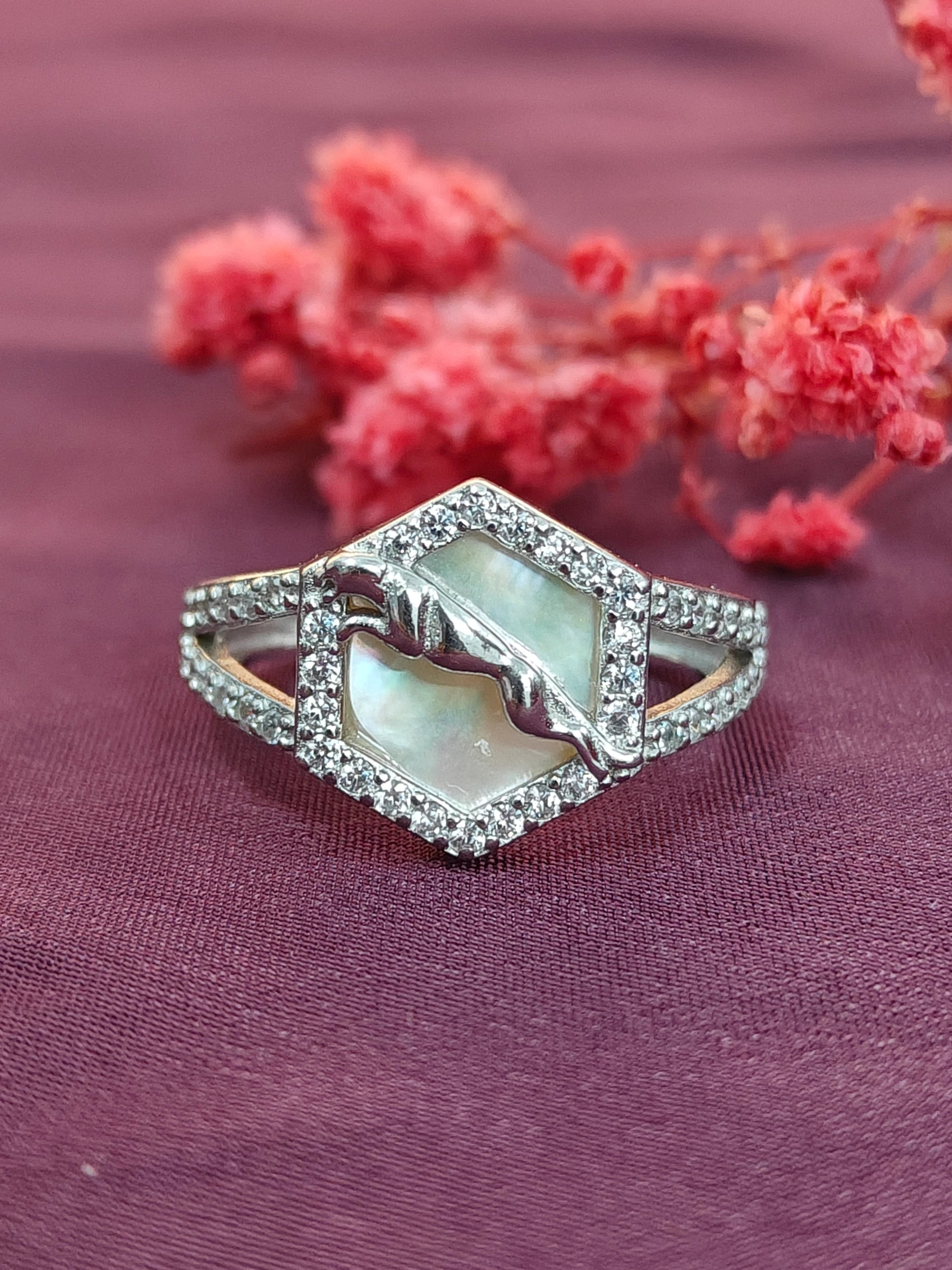 Silver ring with a central gemstone on a purple fabric background with pink flowers.