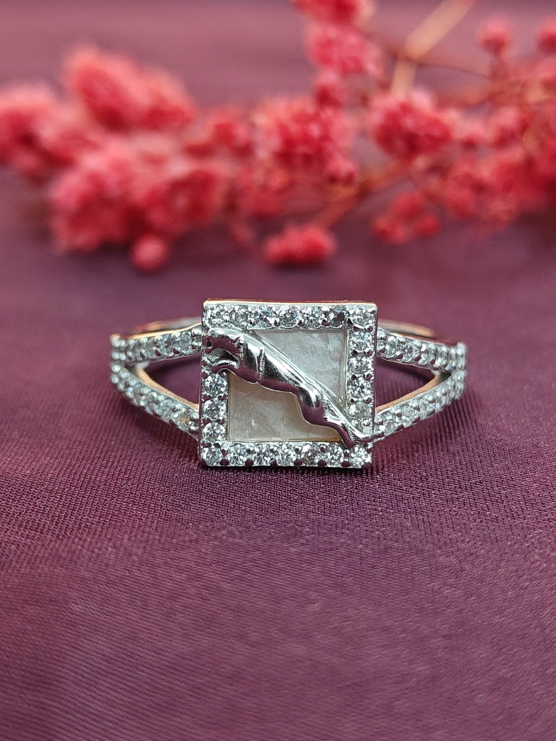 Silver ring with a central stone on a purple fabric background with red flowers.