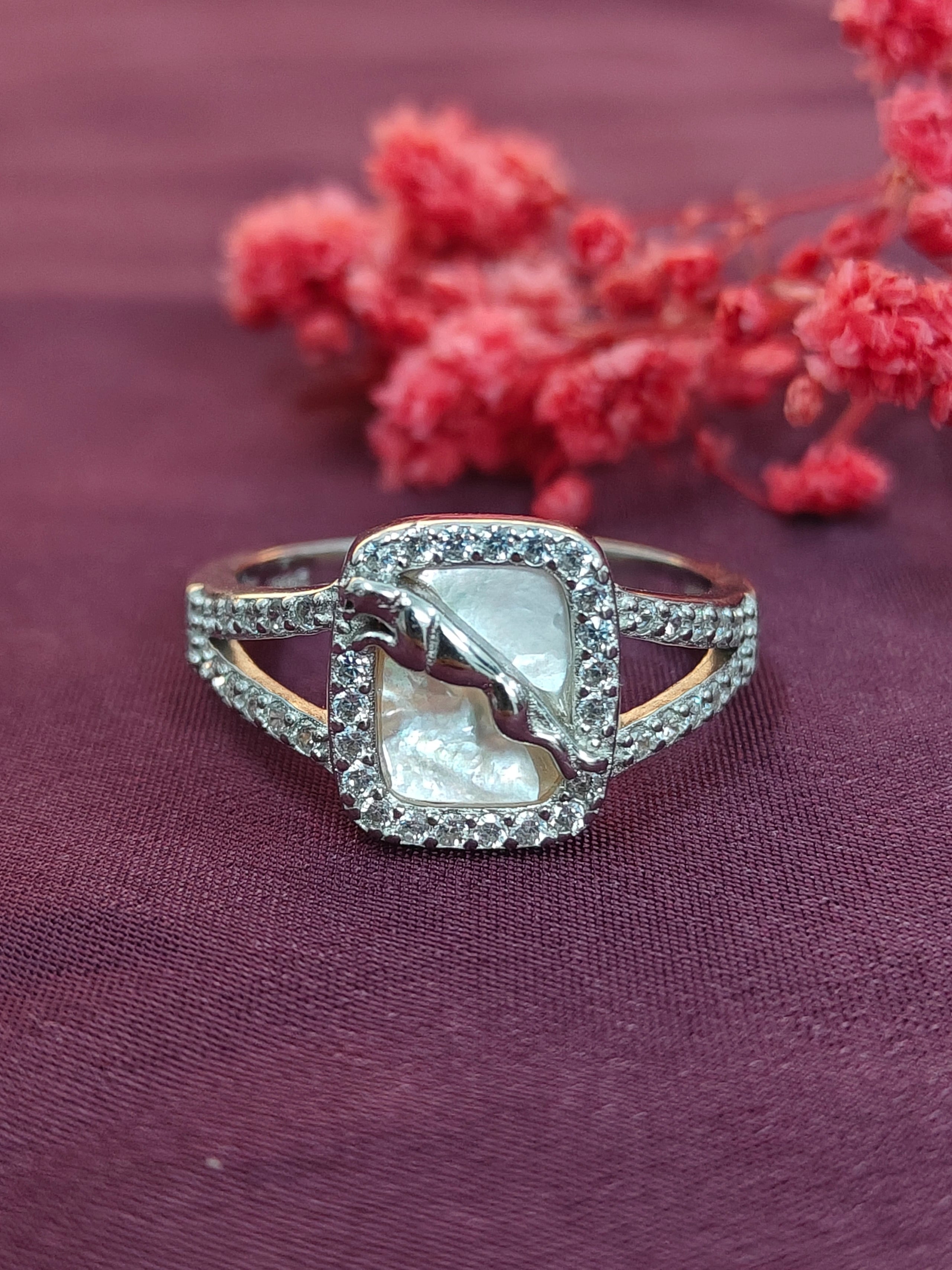 Silver ring with a pearl-like center on a purple fabric background with red flowers.