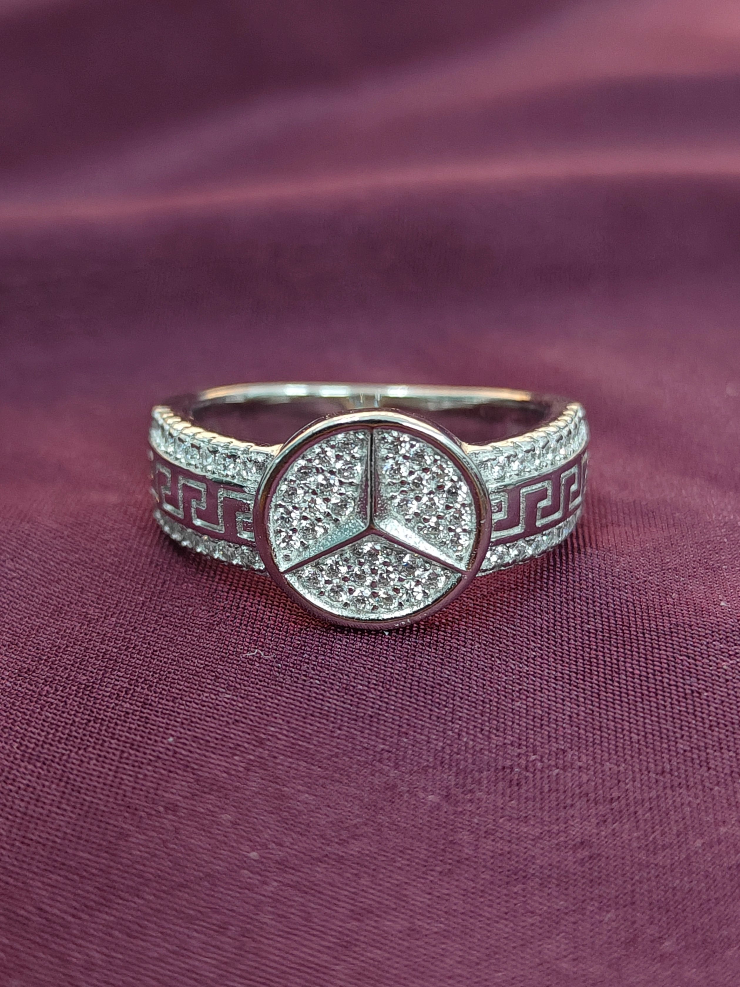 Silver ring with a Mercedes-Benz emblem on a purple fabric background