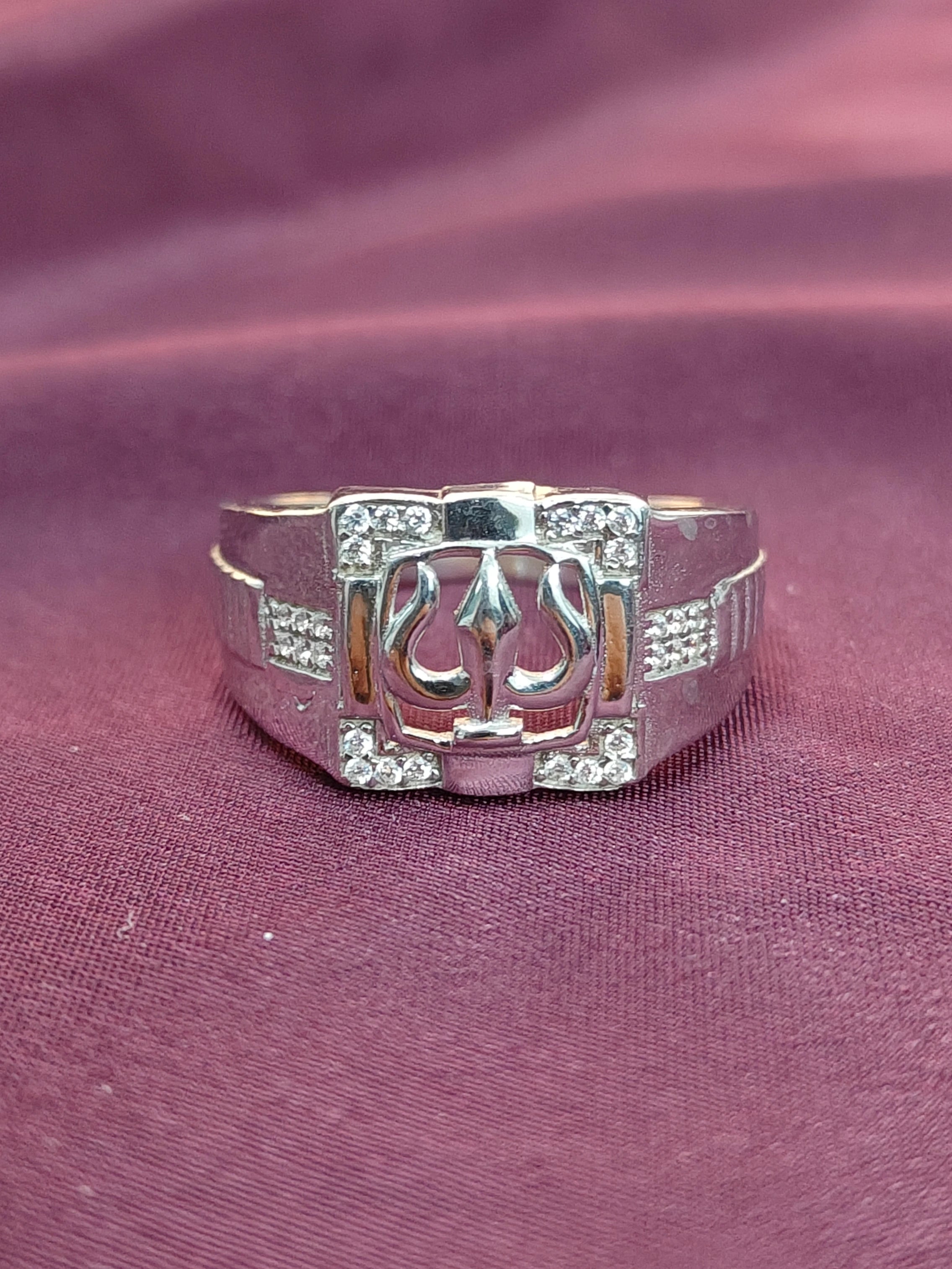 Silver ring with a central emblem on a maroon fabric background