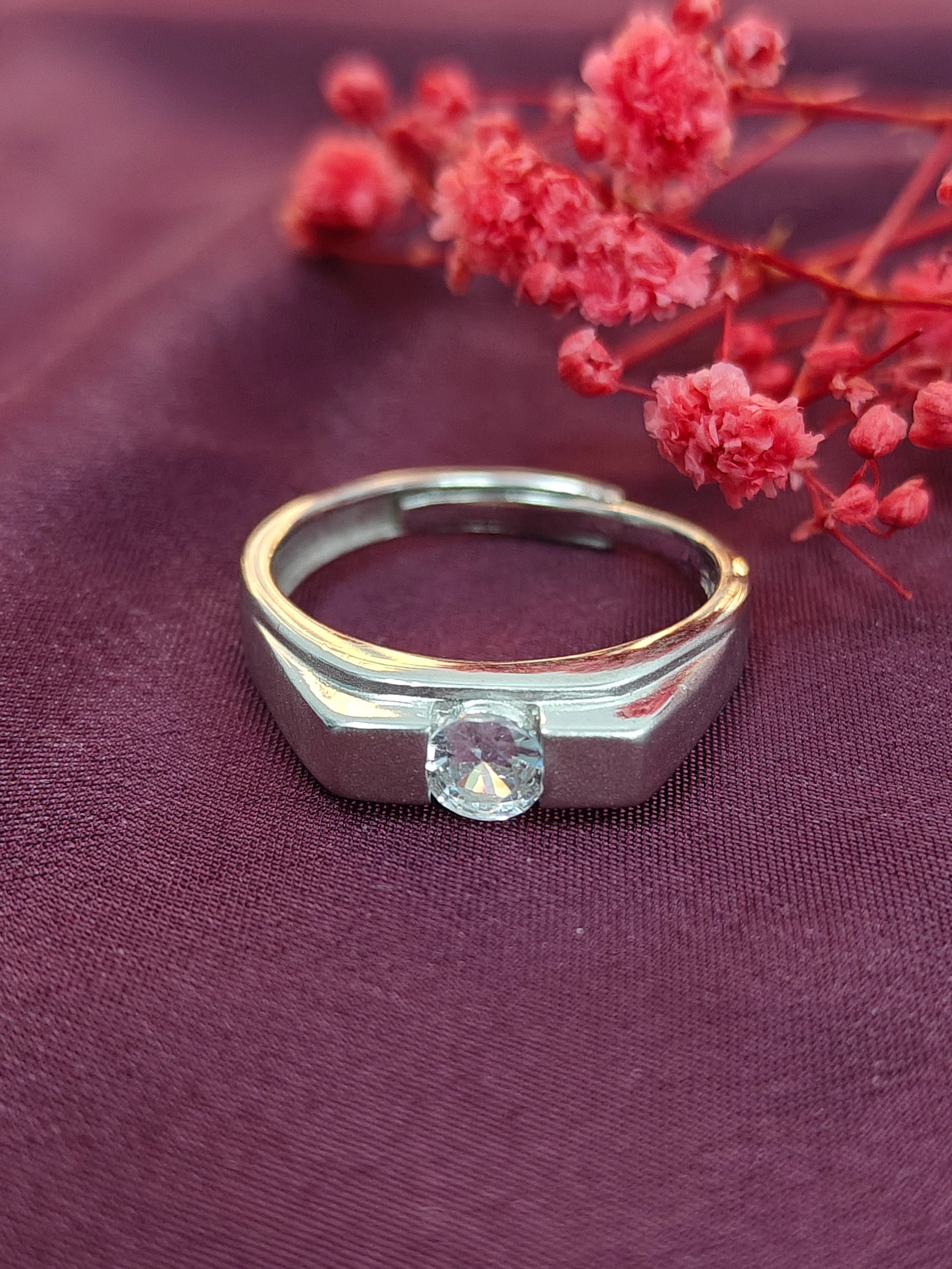 Silver ring with a diamond on a purple fabric background with red flowers.