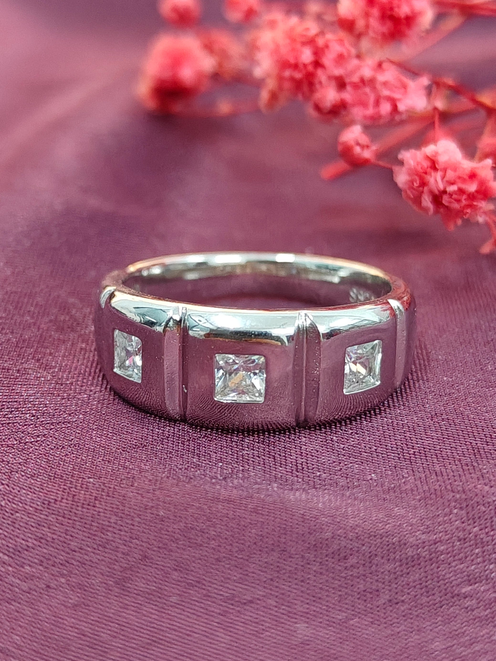 Silver ring with square-cut gemstones on a pink fabric background