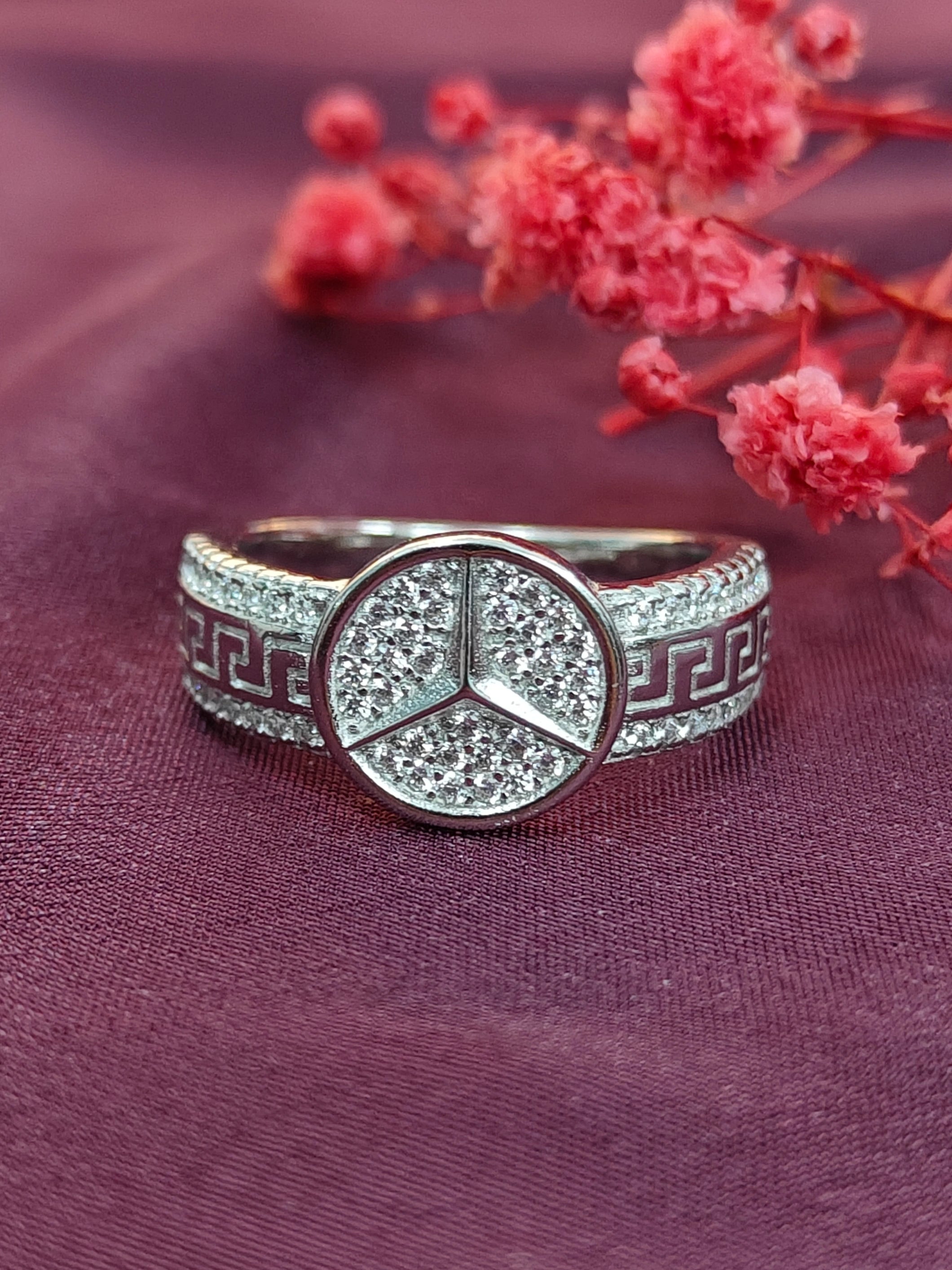 Silver ring with a central emblem on a purple fabric background with red flowers.