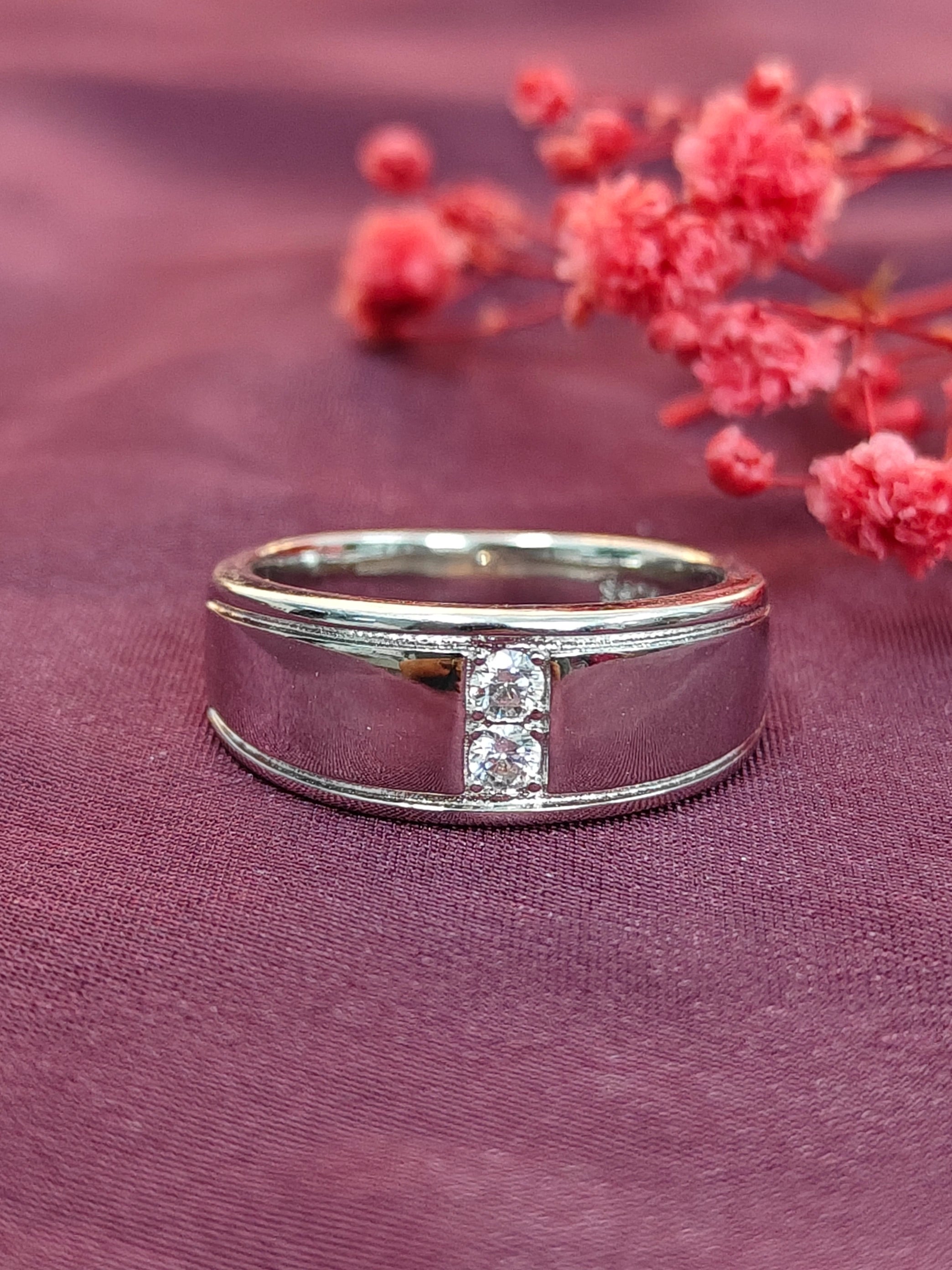Silver ring with a diamond on a purple fabric background with pink flowers.