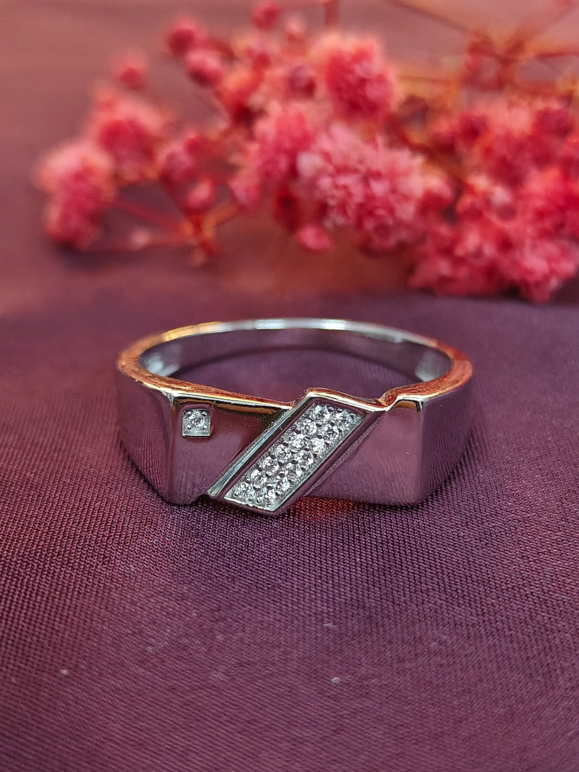 Silver ring with rose gold accents and small diamonds on a purple fabric background with pink flowers.