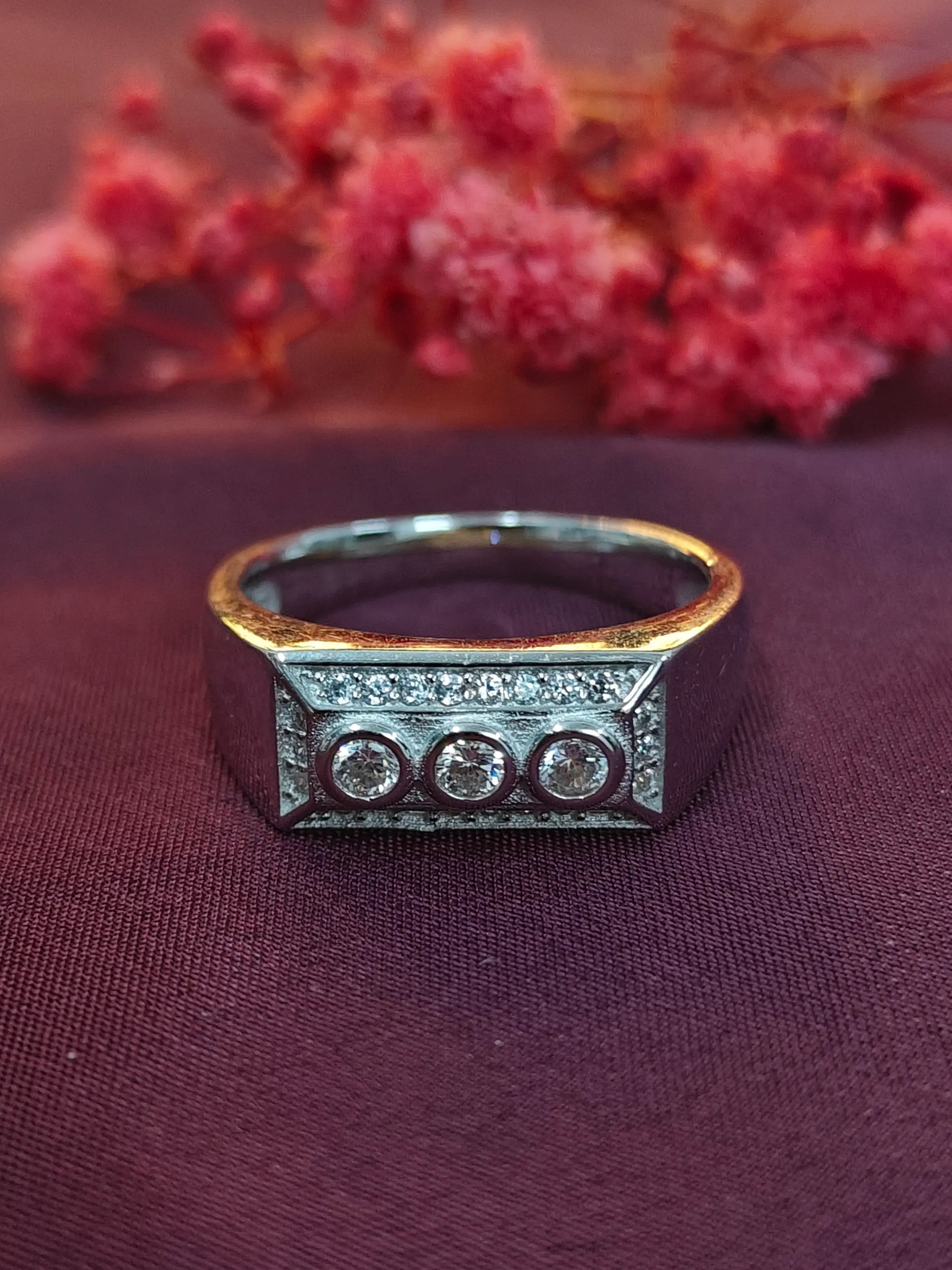 Silver ring with three circular stones on a purple fabric background with red flowers.