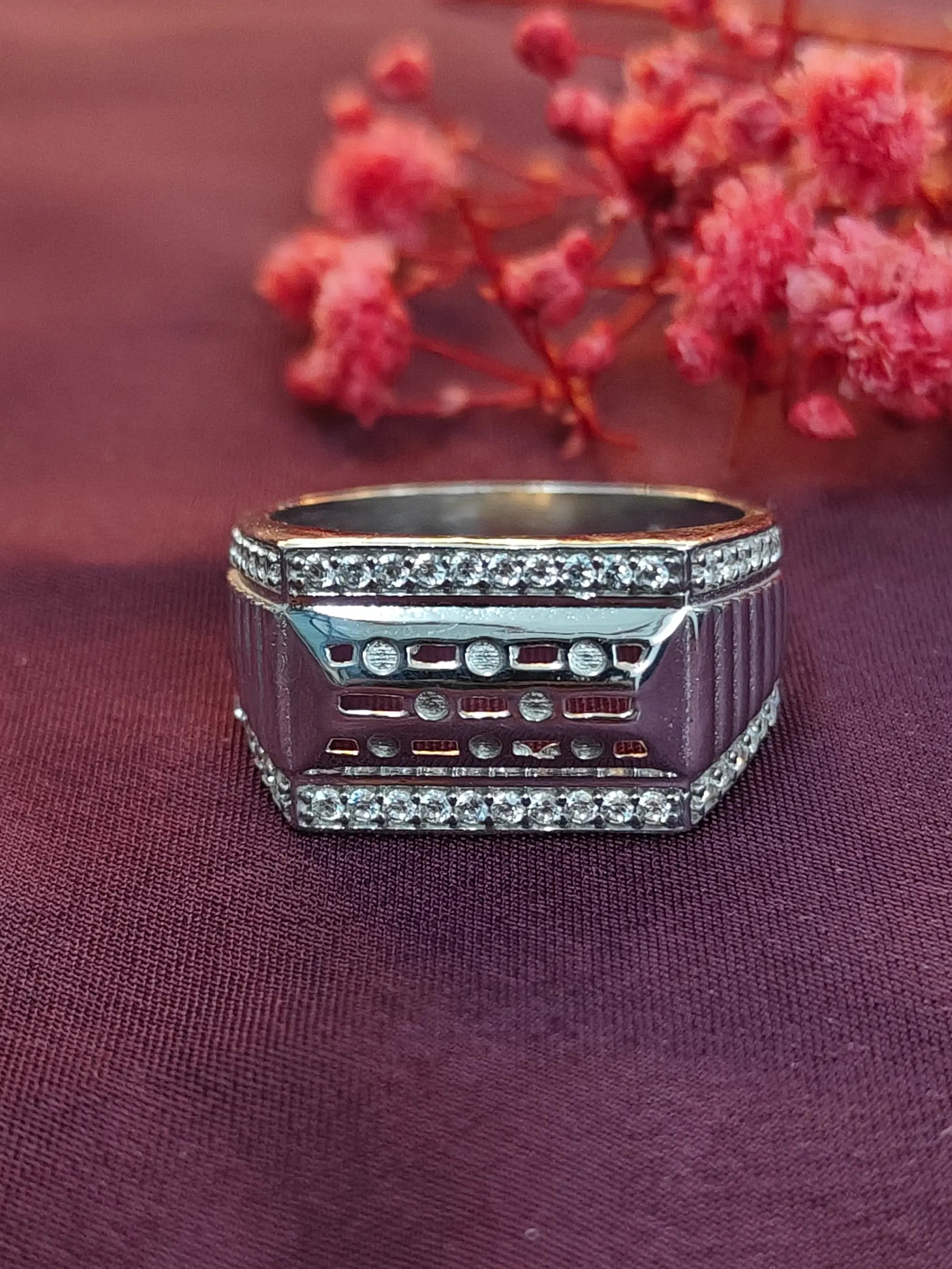Silver ring with gemstones on a purple fabric background with pink flowers.