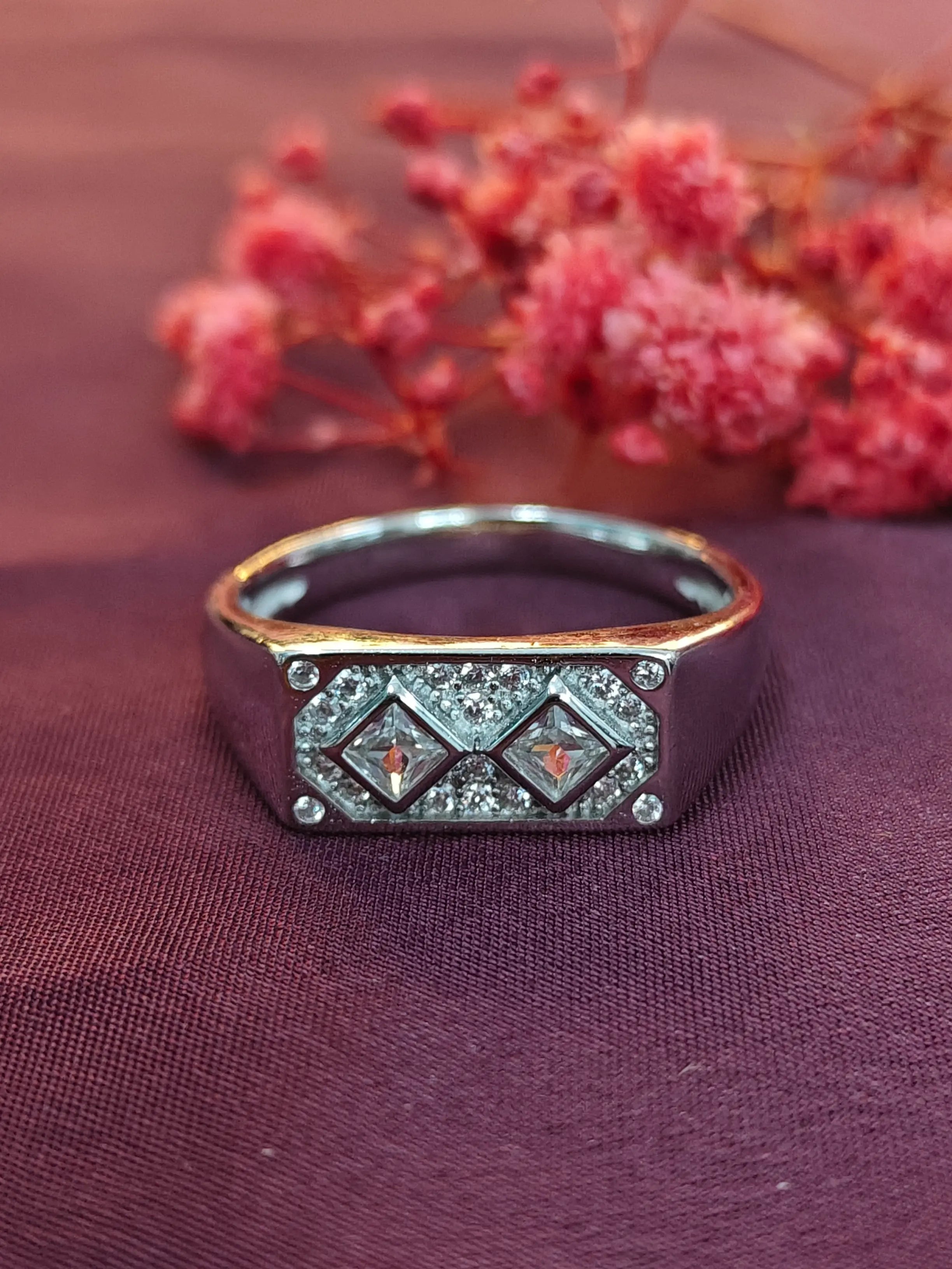 Decorative ring with gemstones on a purple fabric background with pink flowers.