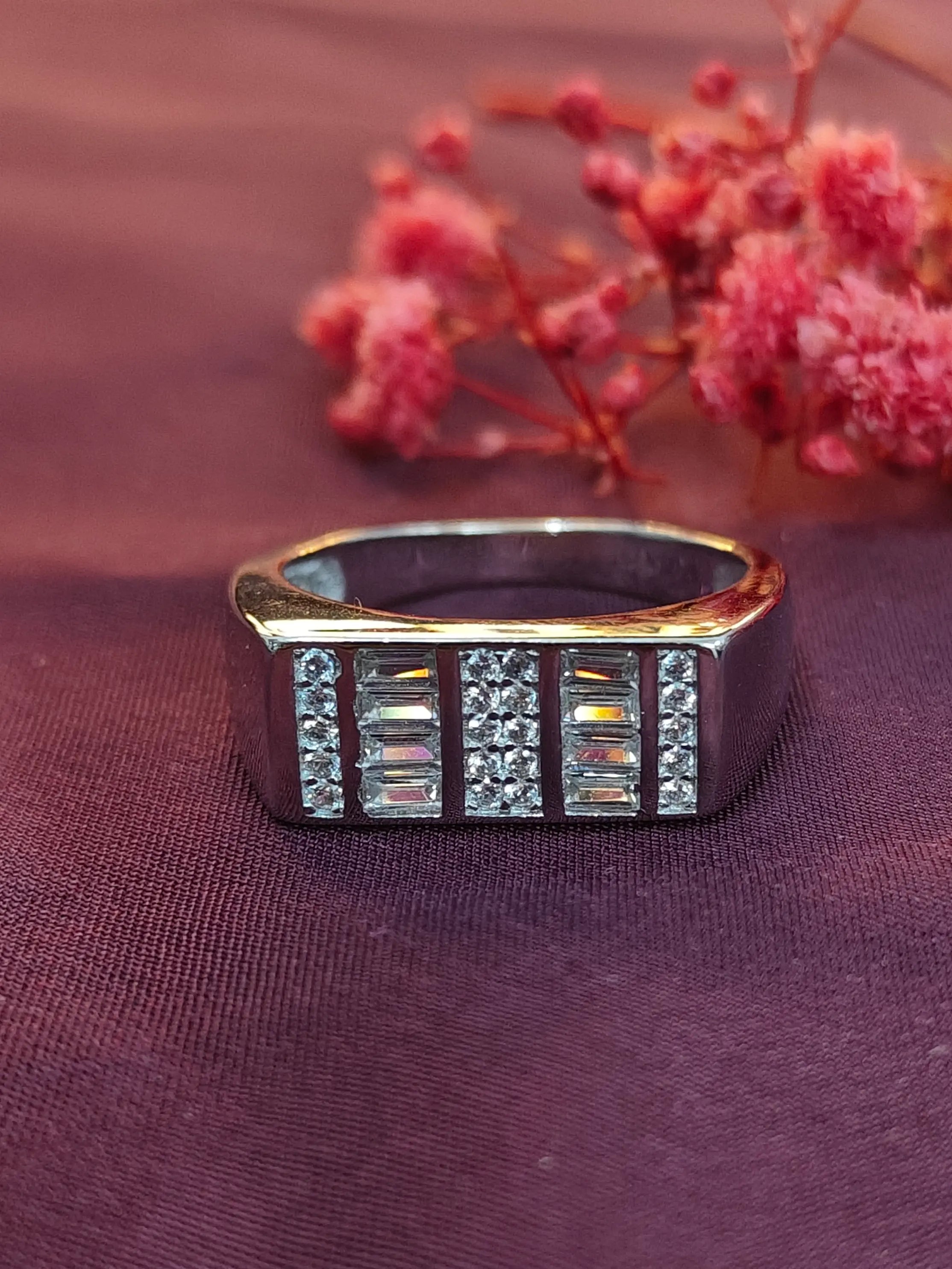 Gold ring with gemstones on a purple fabric background with pink flowers.