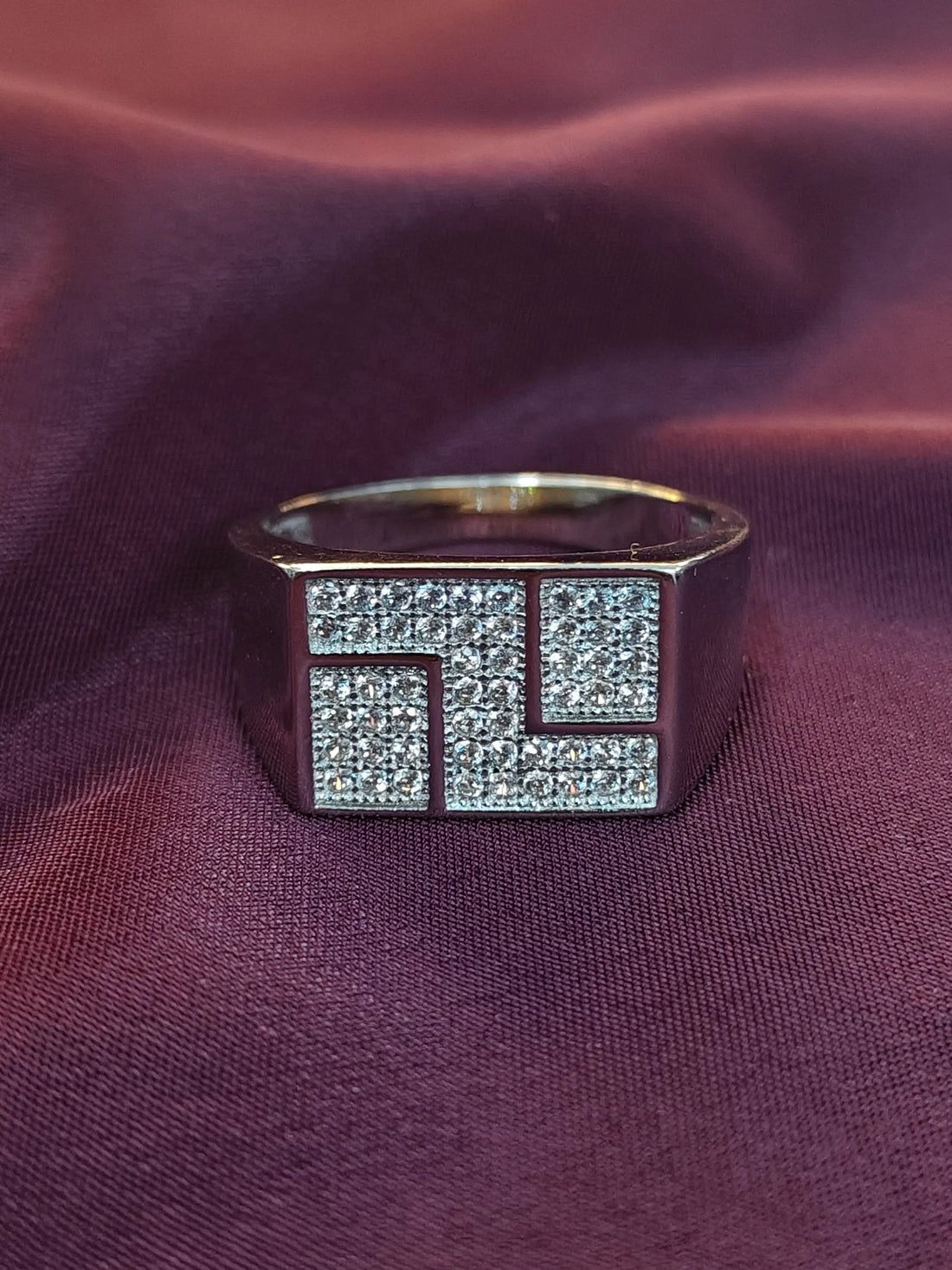 Silver ring with geometric diamond design on a purple fabric background