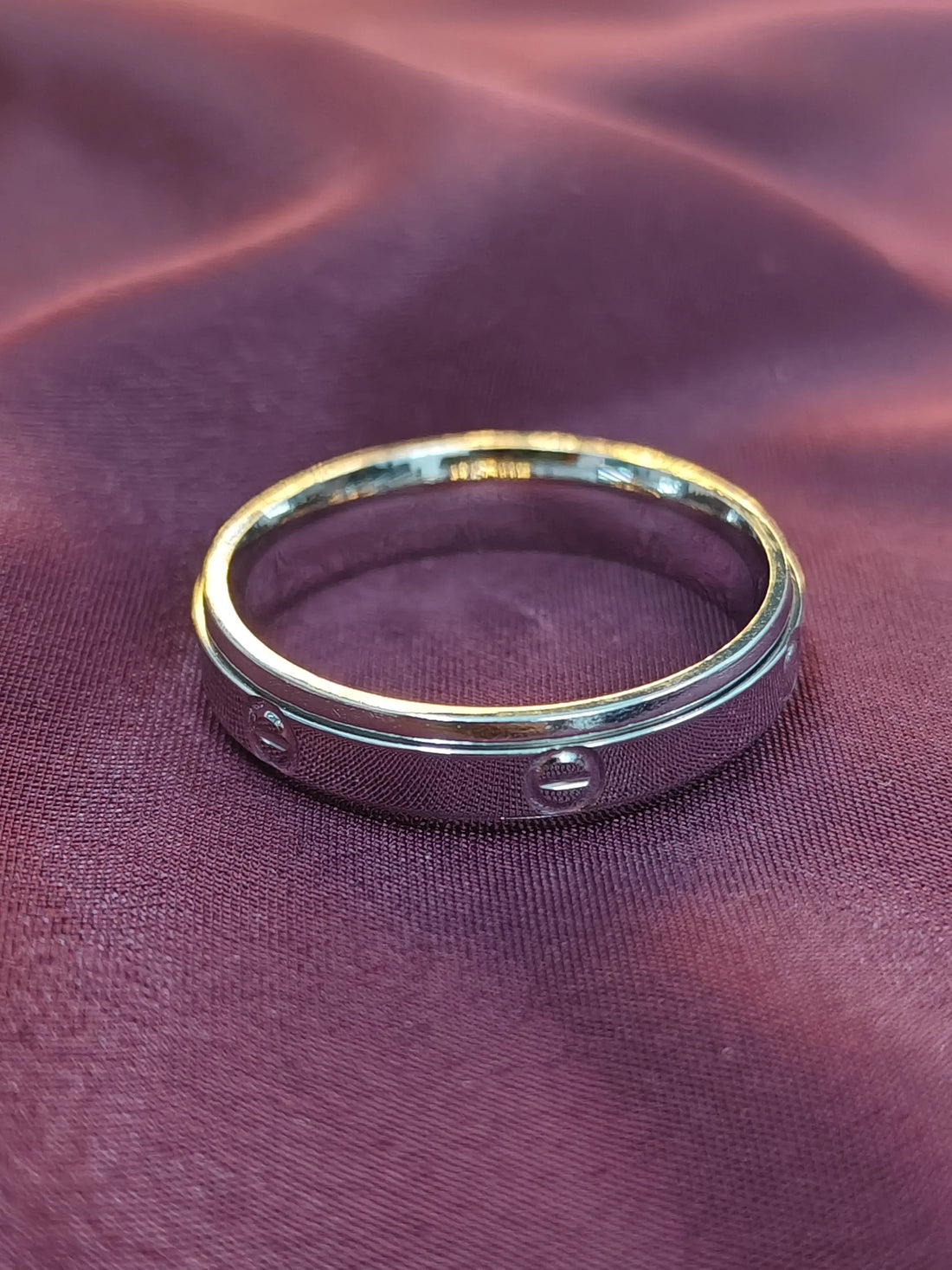 Silver ring with engraved text on a purple fabric background