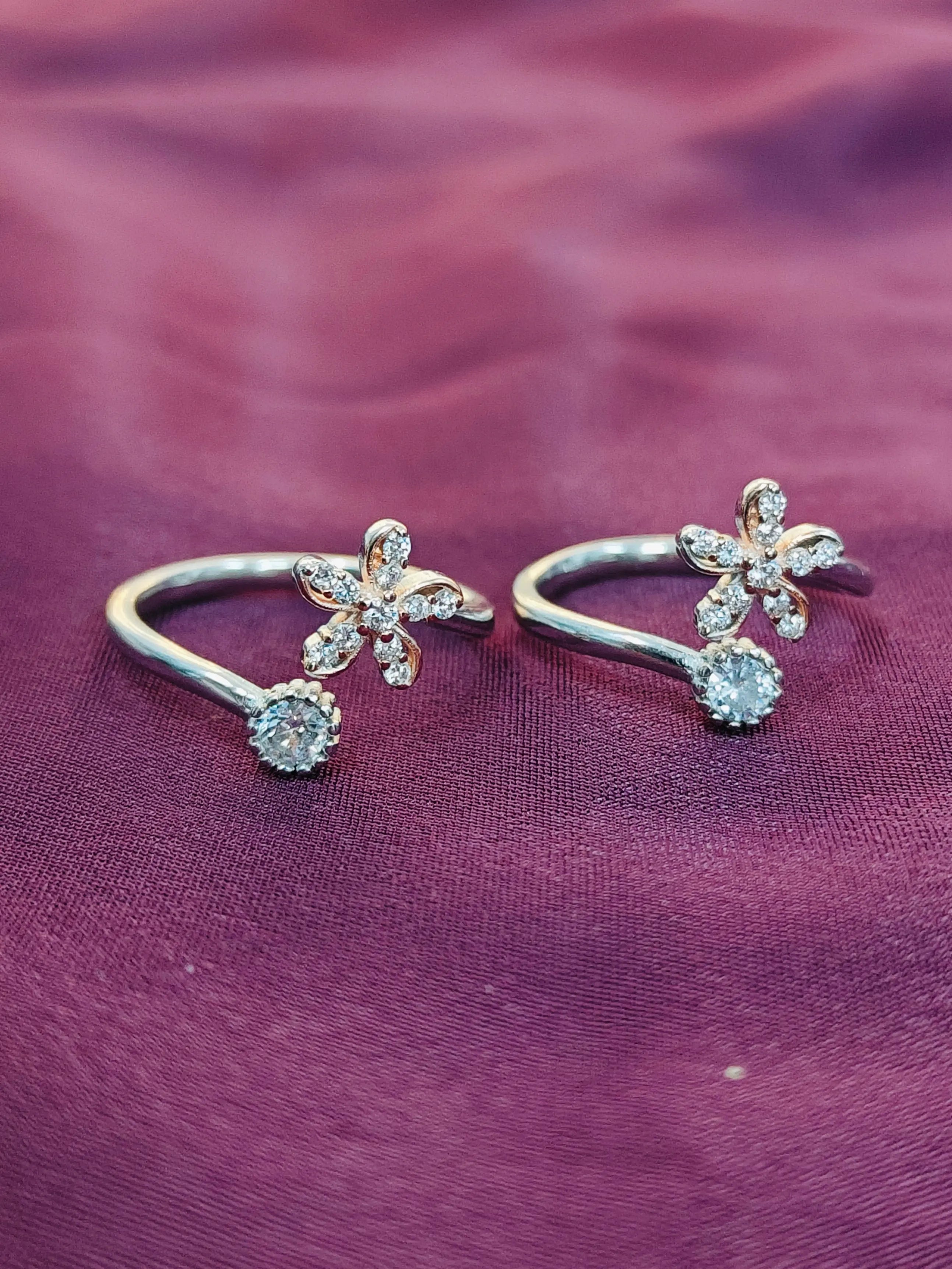 Pair of silver floral earrings with clear stones on a purple fabric background