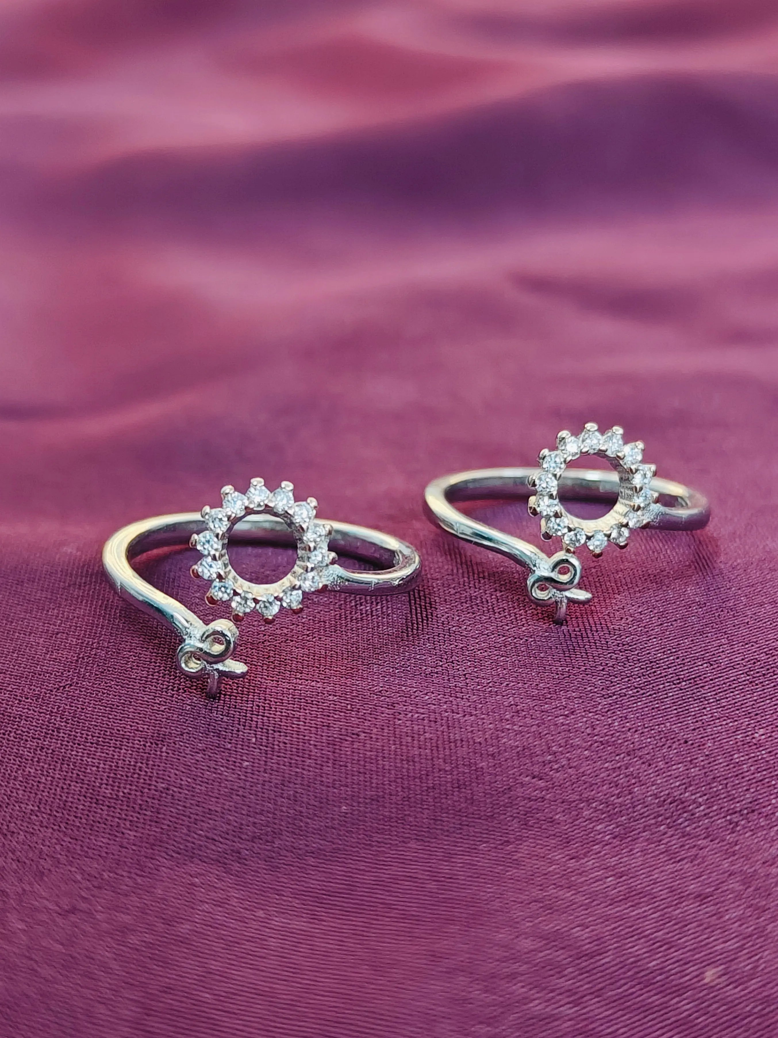 Pair of silver rings with heart-shaped diamond designs on a purple fabric background