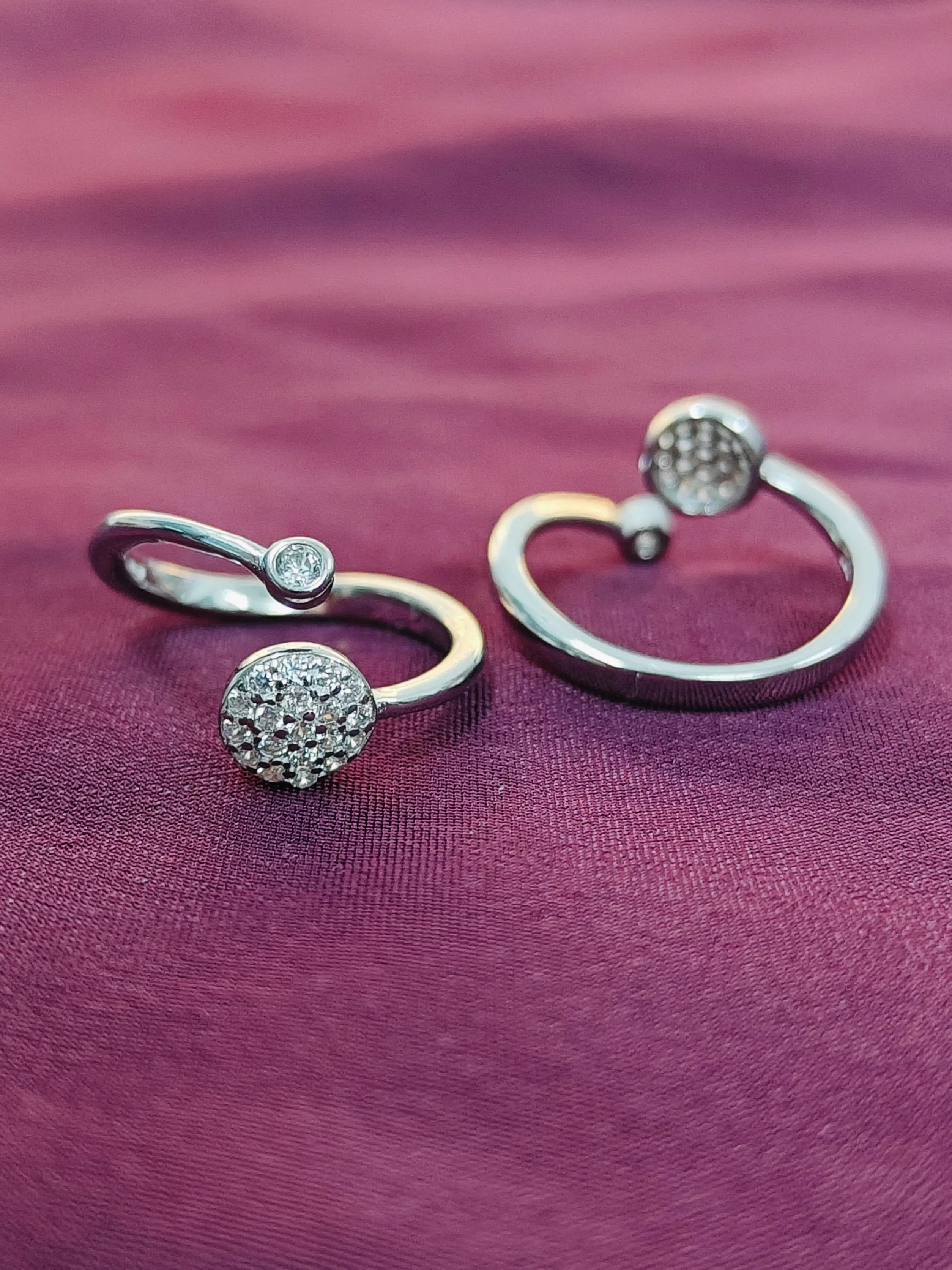 Two silver rings with gemstone accents on a purple fabric background