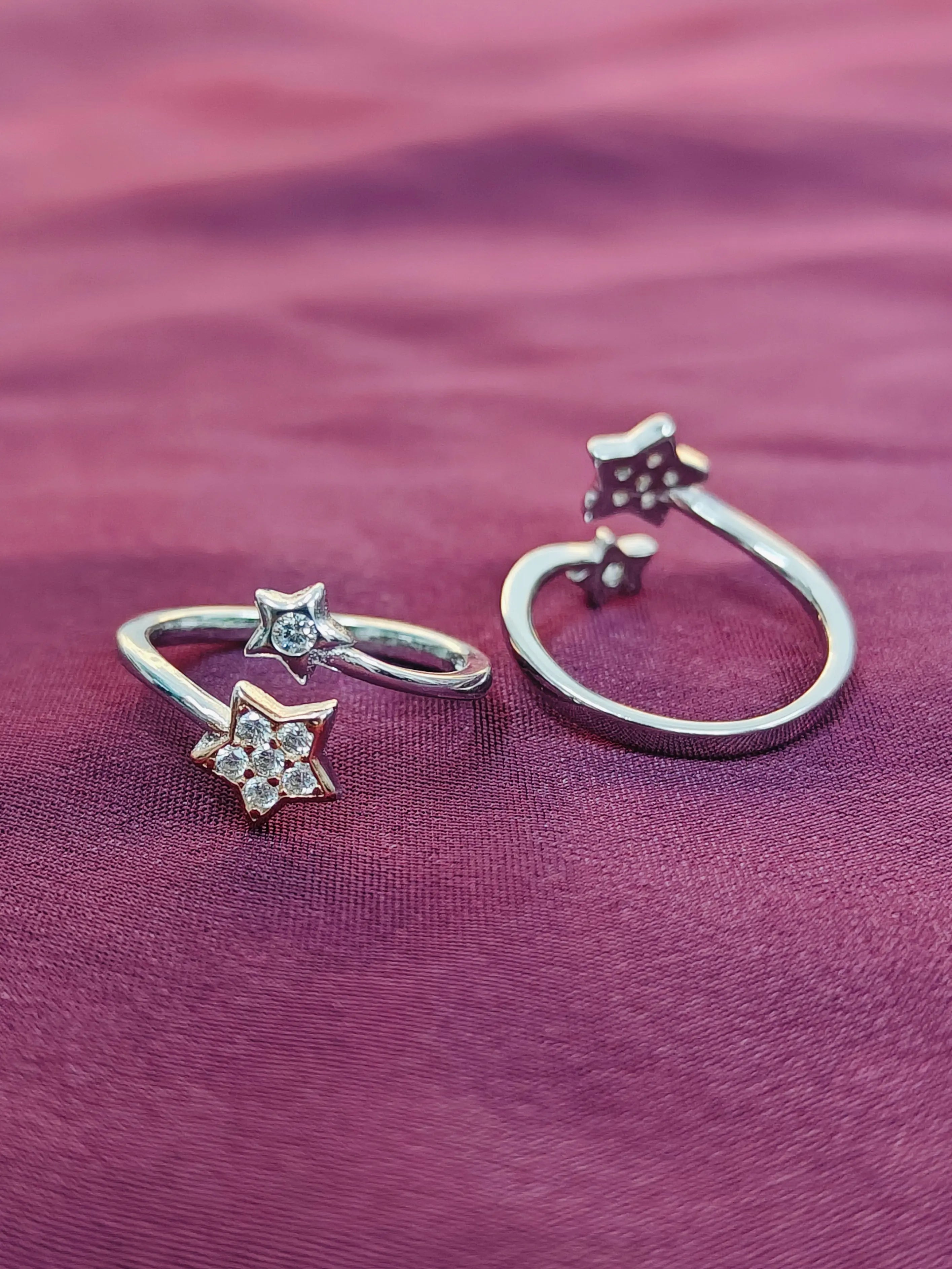 Two silver rings with star designs on a purple fabric background
