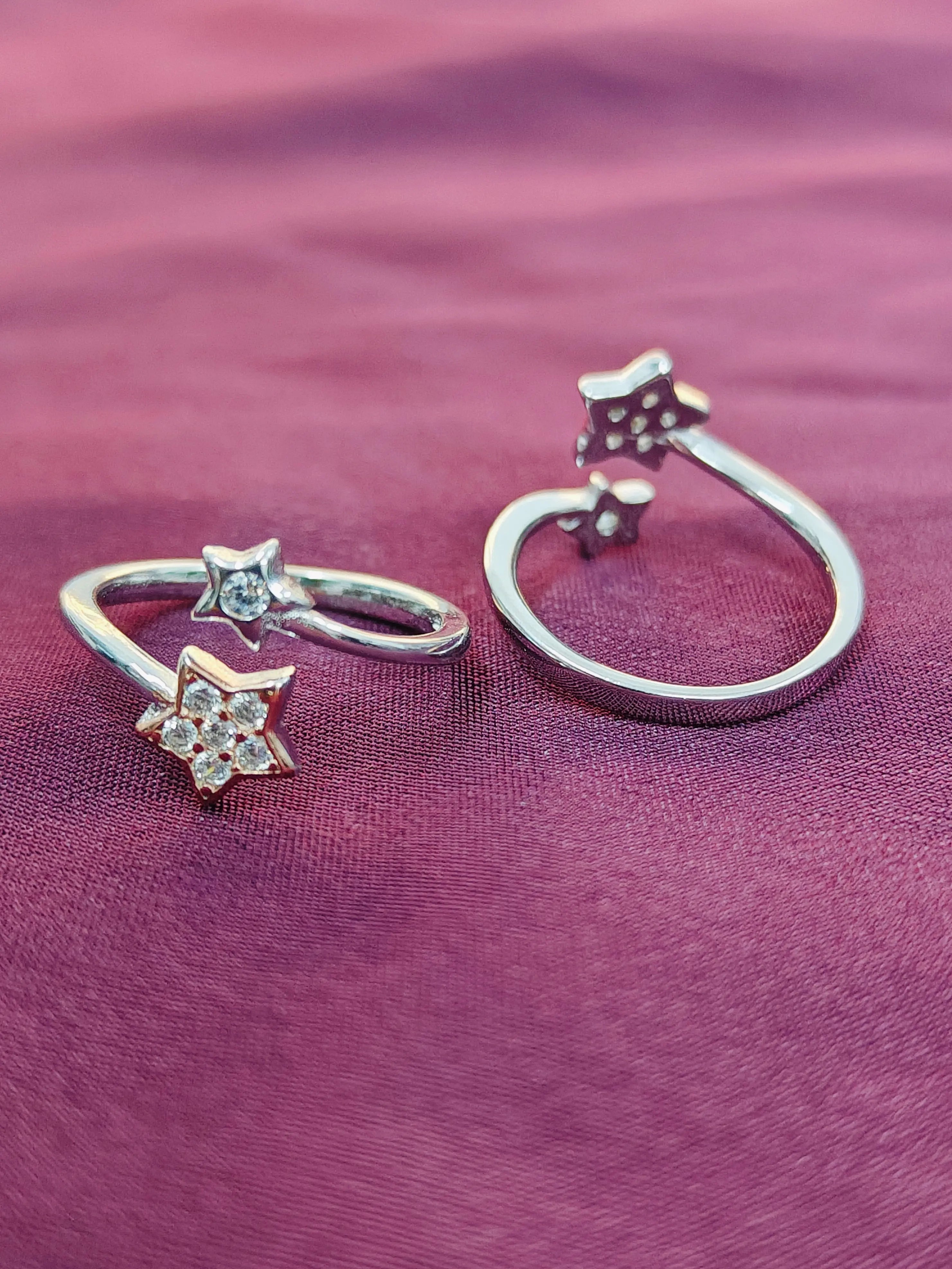 Two silver star-shaped rings on a purple fabric background
