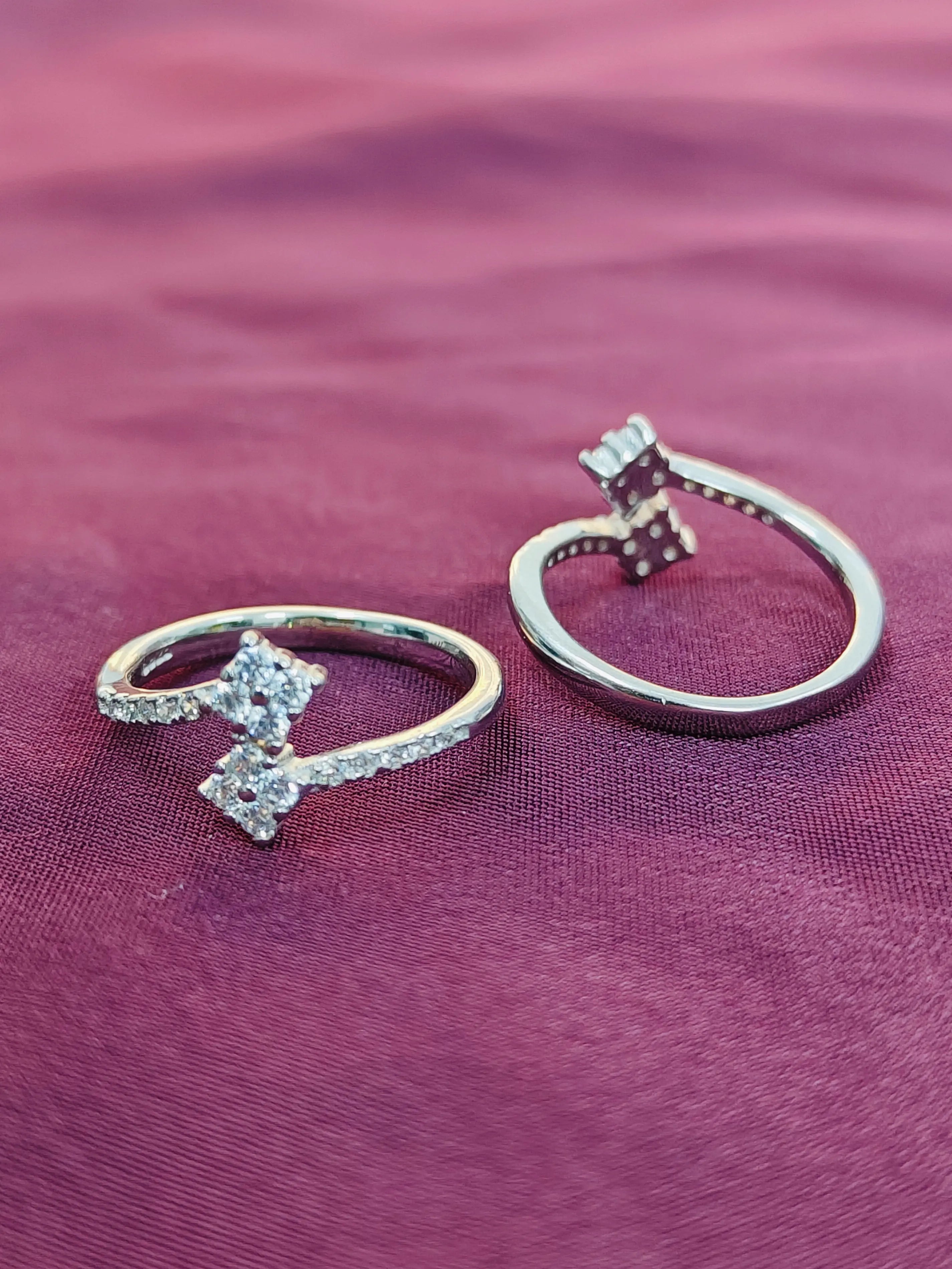 Two silver rings with diamond accents on a purple fabric background