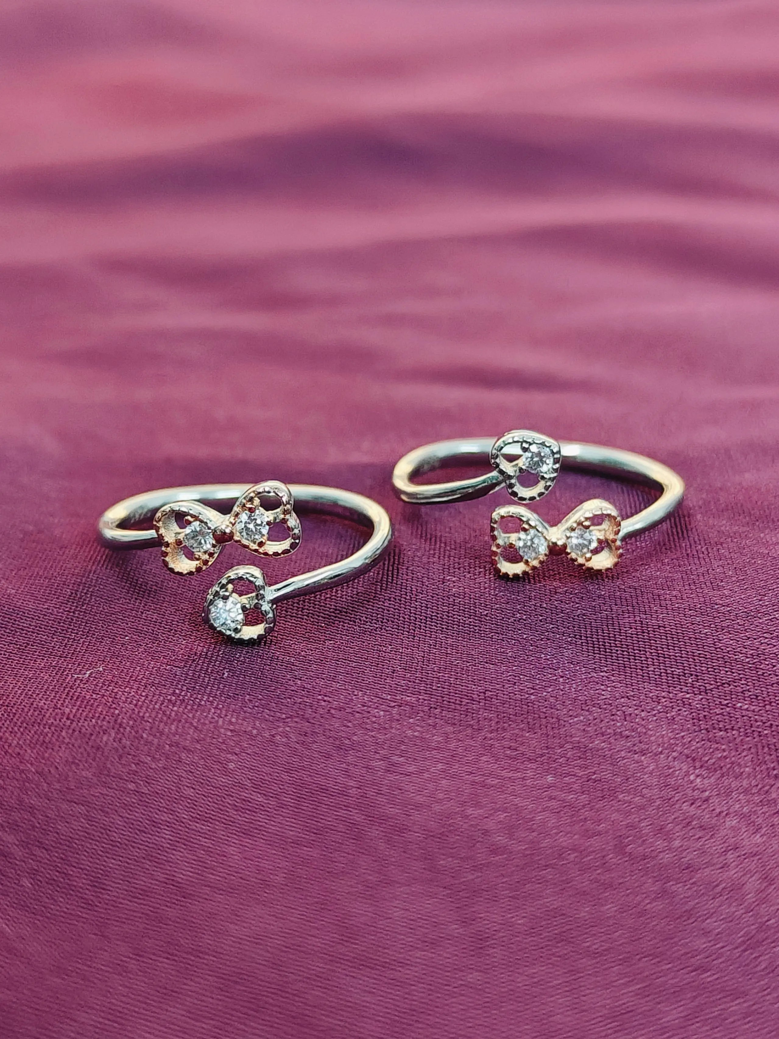 Two silver rings with bow designs on a purple fabric background
