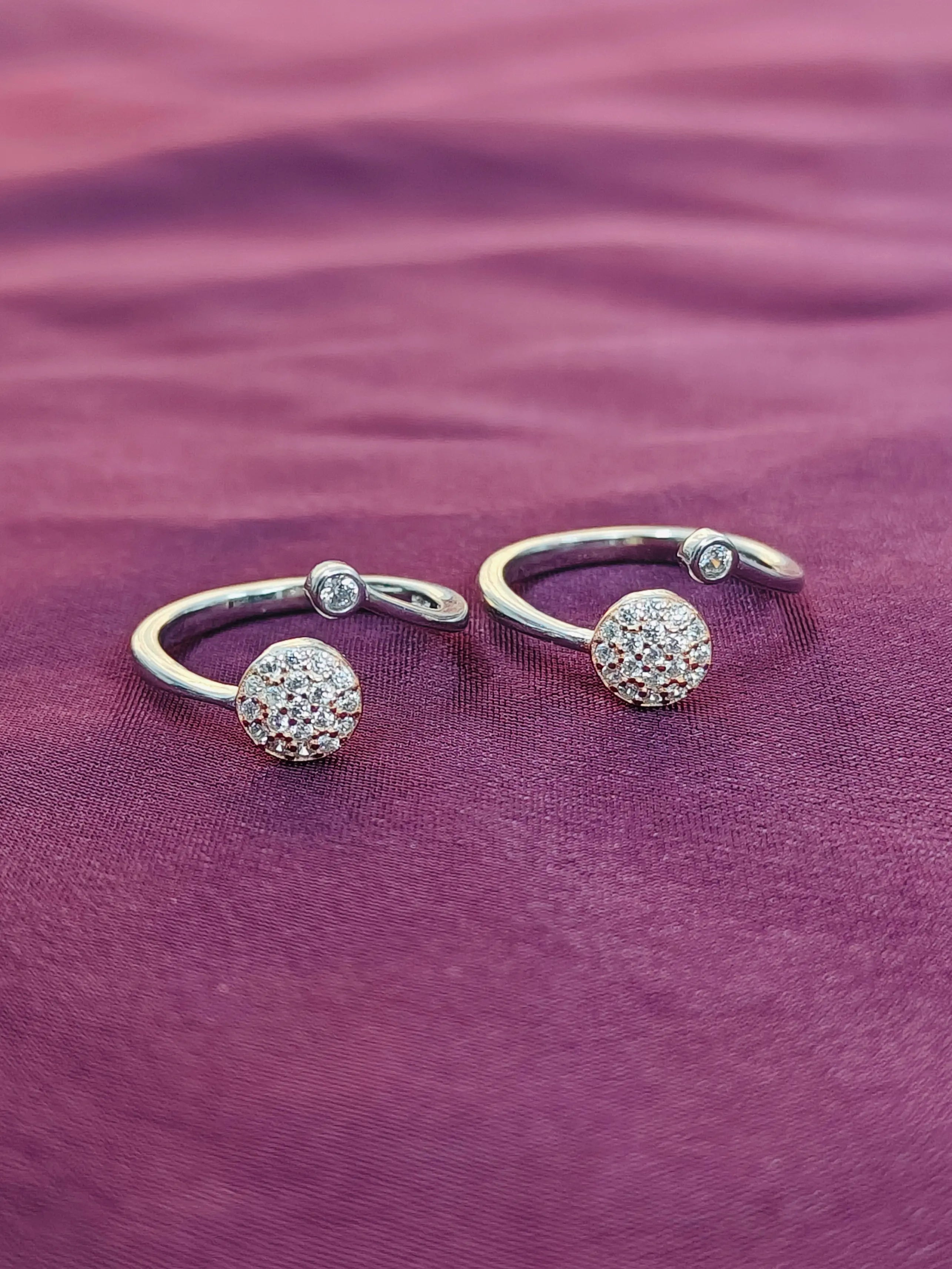 Two silver open rings with spherical ends on a purple fabric background