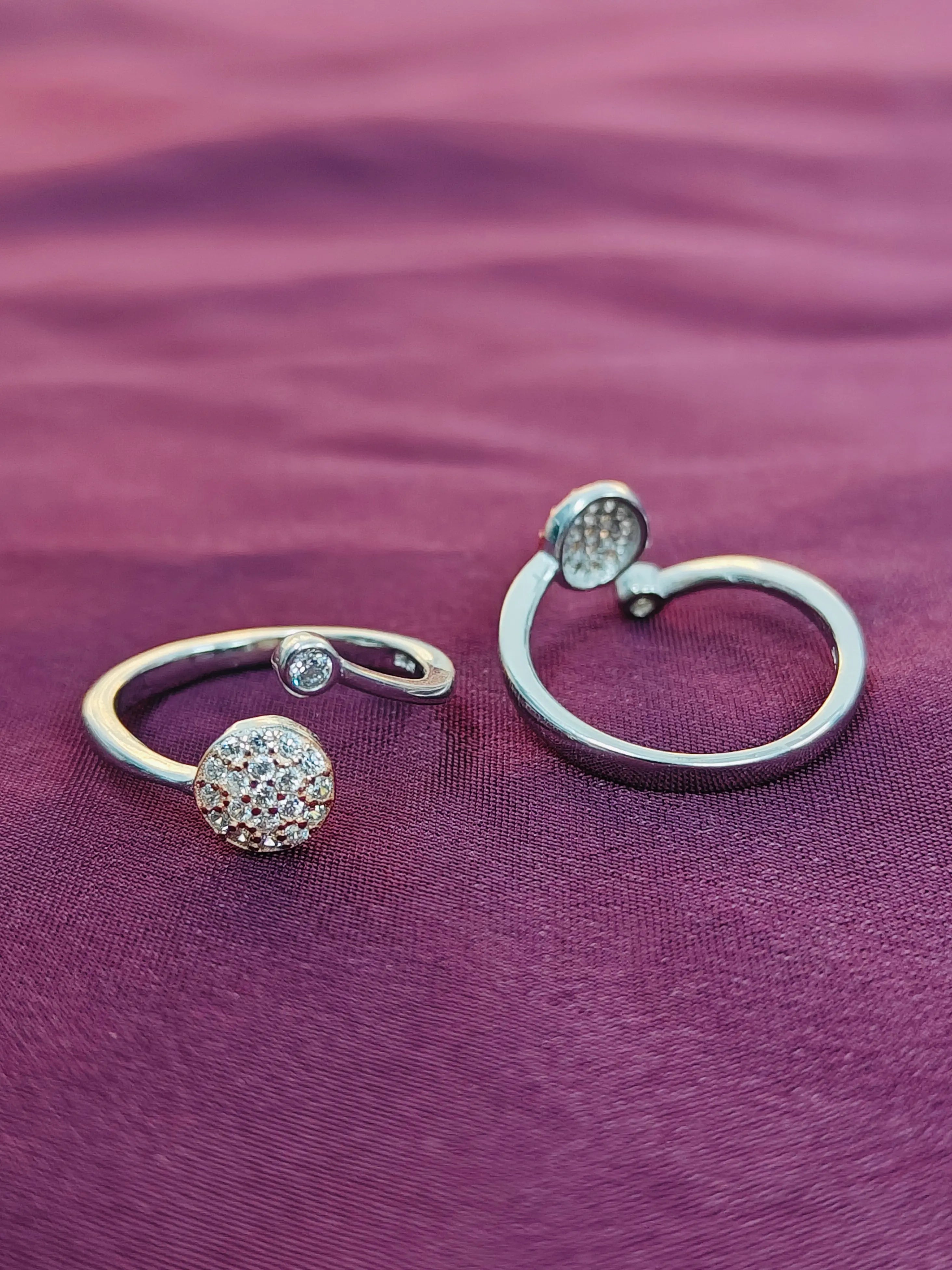 Two silver rings with gemstone accents on a purple fabric background
