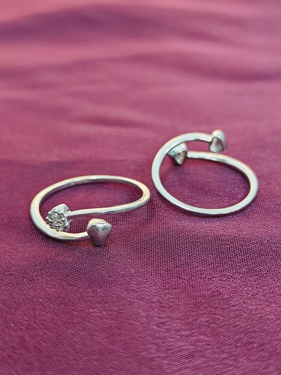 Silver hoop earrings with heart and diamond-shaped charms on a purple fabric background