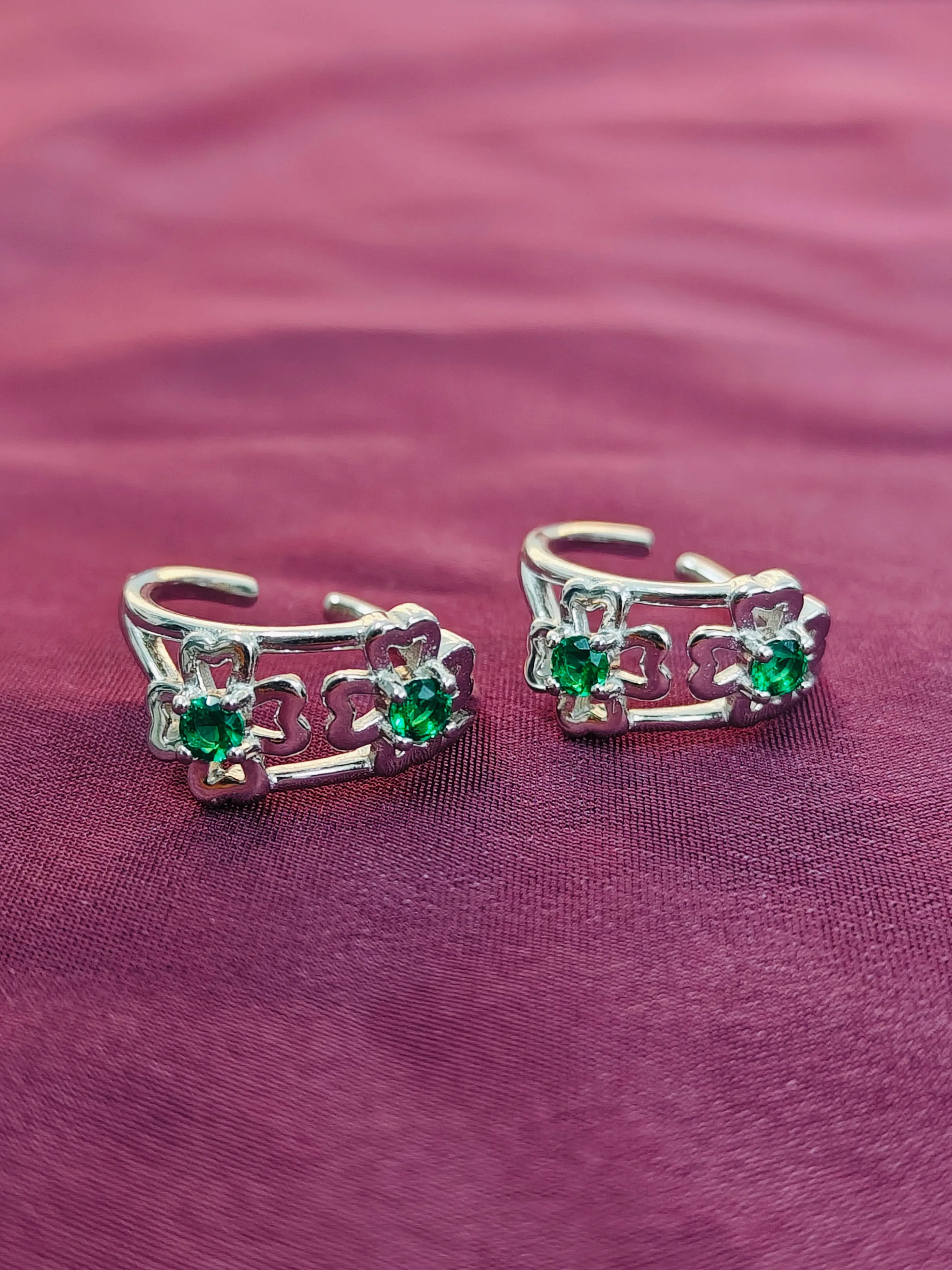 Pair of silver ear cuffs with green gemstones on a purple fabric background