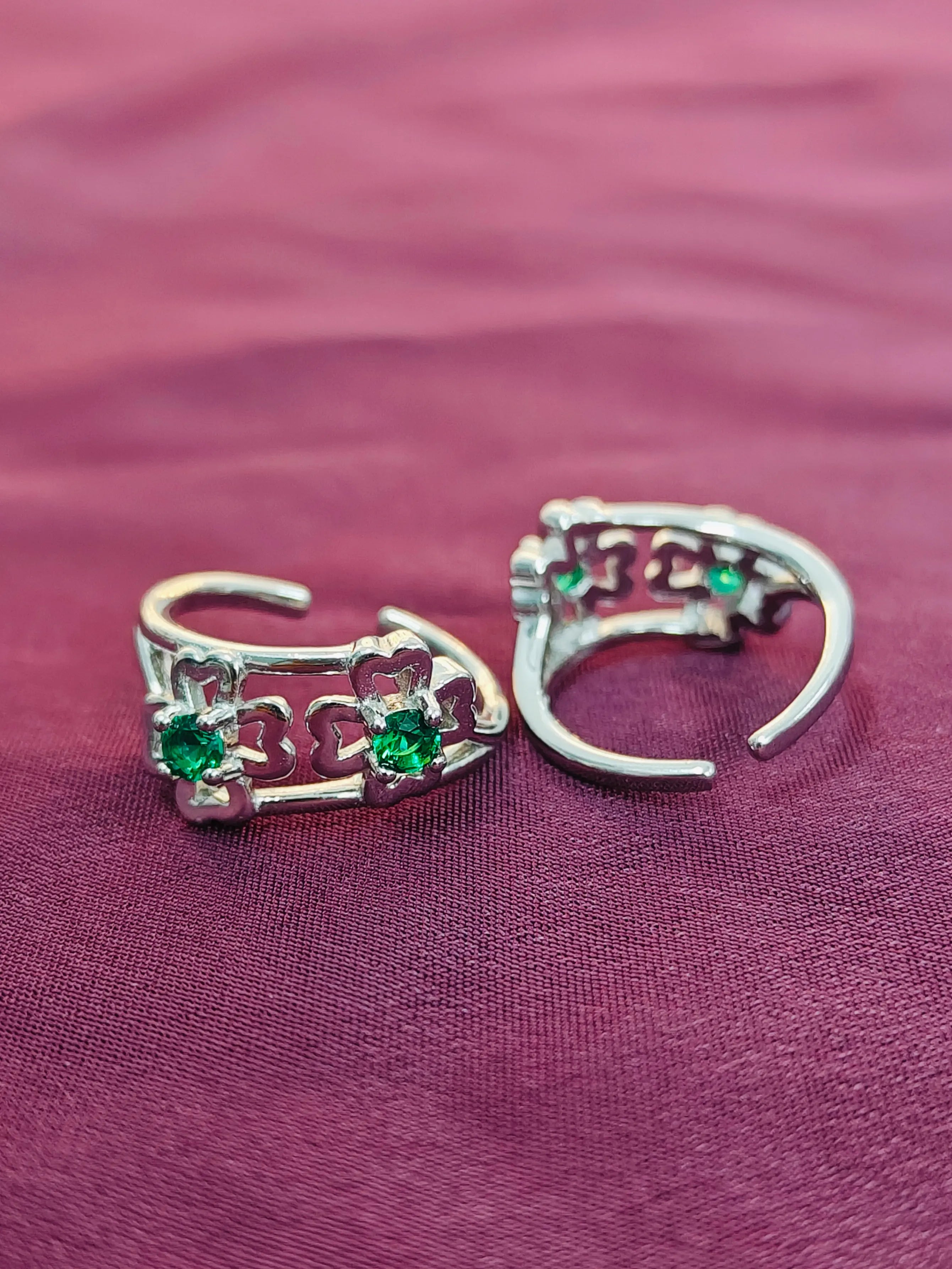 Two silver rings with green gemstones on a purple fabric background